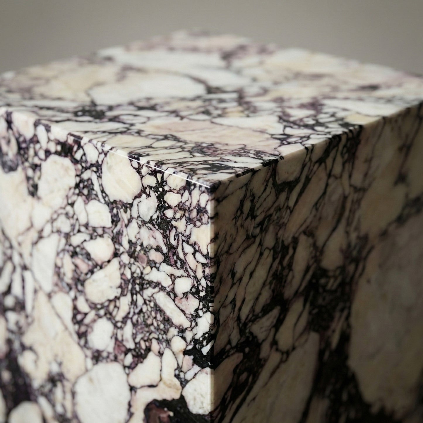 An extreme close-up of the corner of a Calacatta Viola marble pedestal, showcasing the precision-mitered edge and the intricate natural patterns of deep purple and cream-colored stone.