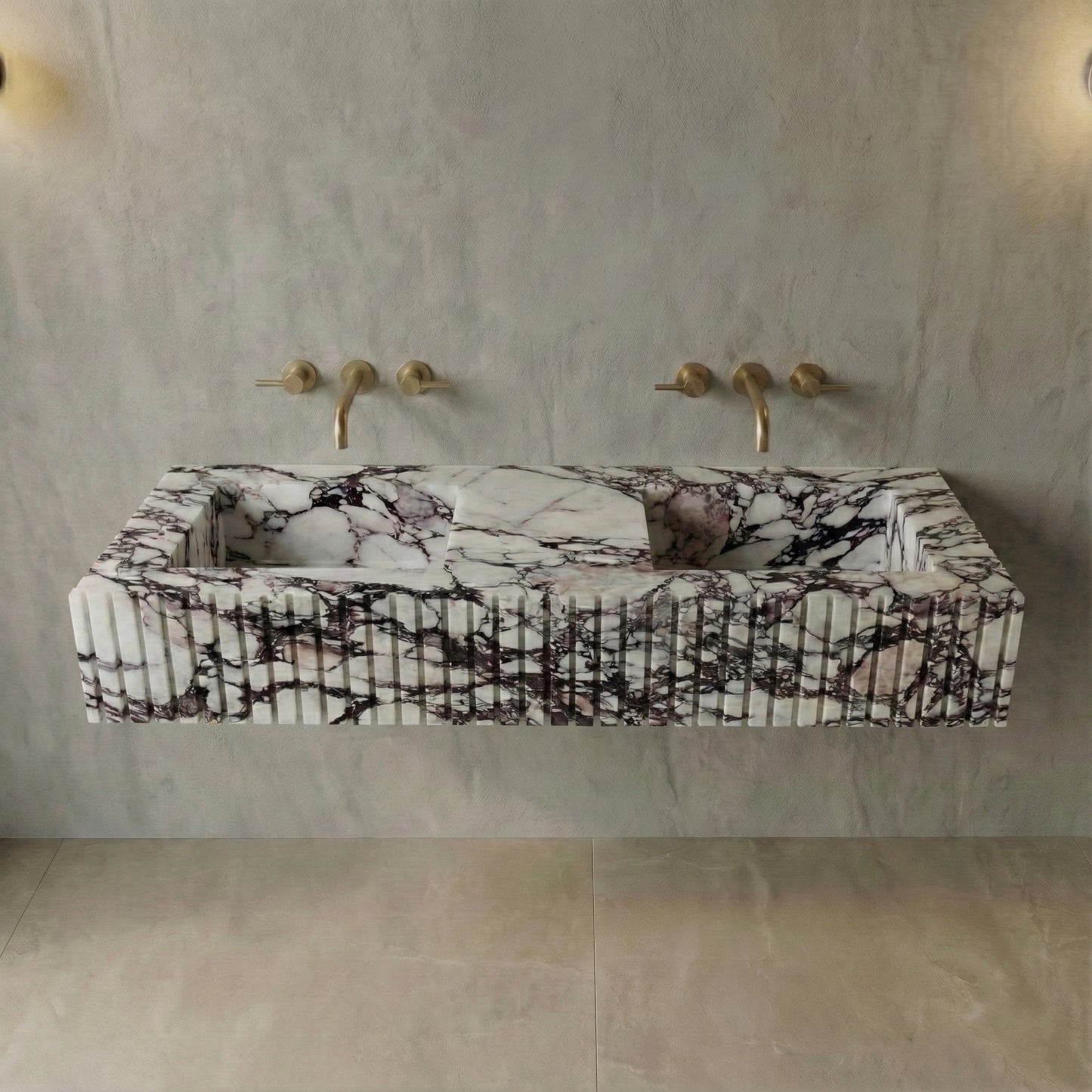 Front profile of a floating Calacatta Viola marble double vanity featuring a custom fluted stone apron and wall-mounted brushed gold faucets.