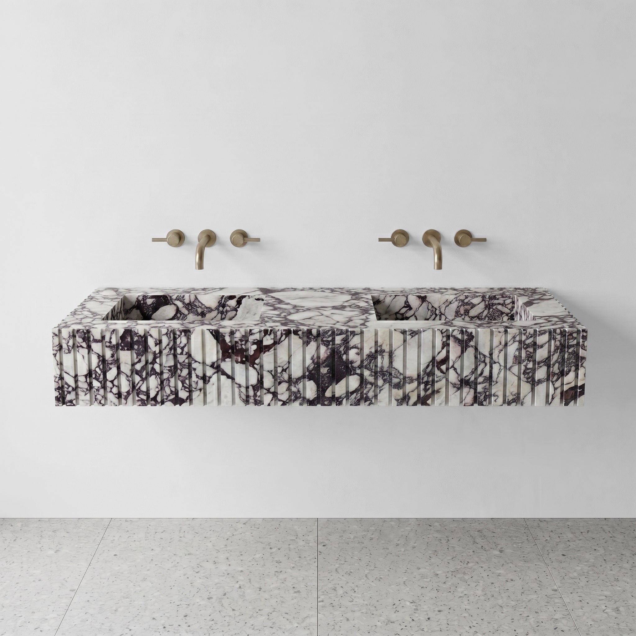Front profile of a floating Calacatta Viola marble double vanity featuring a custom fluted stone apron and wall-mounted brushed gold faucets.