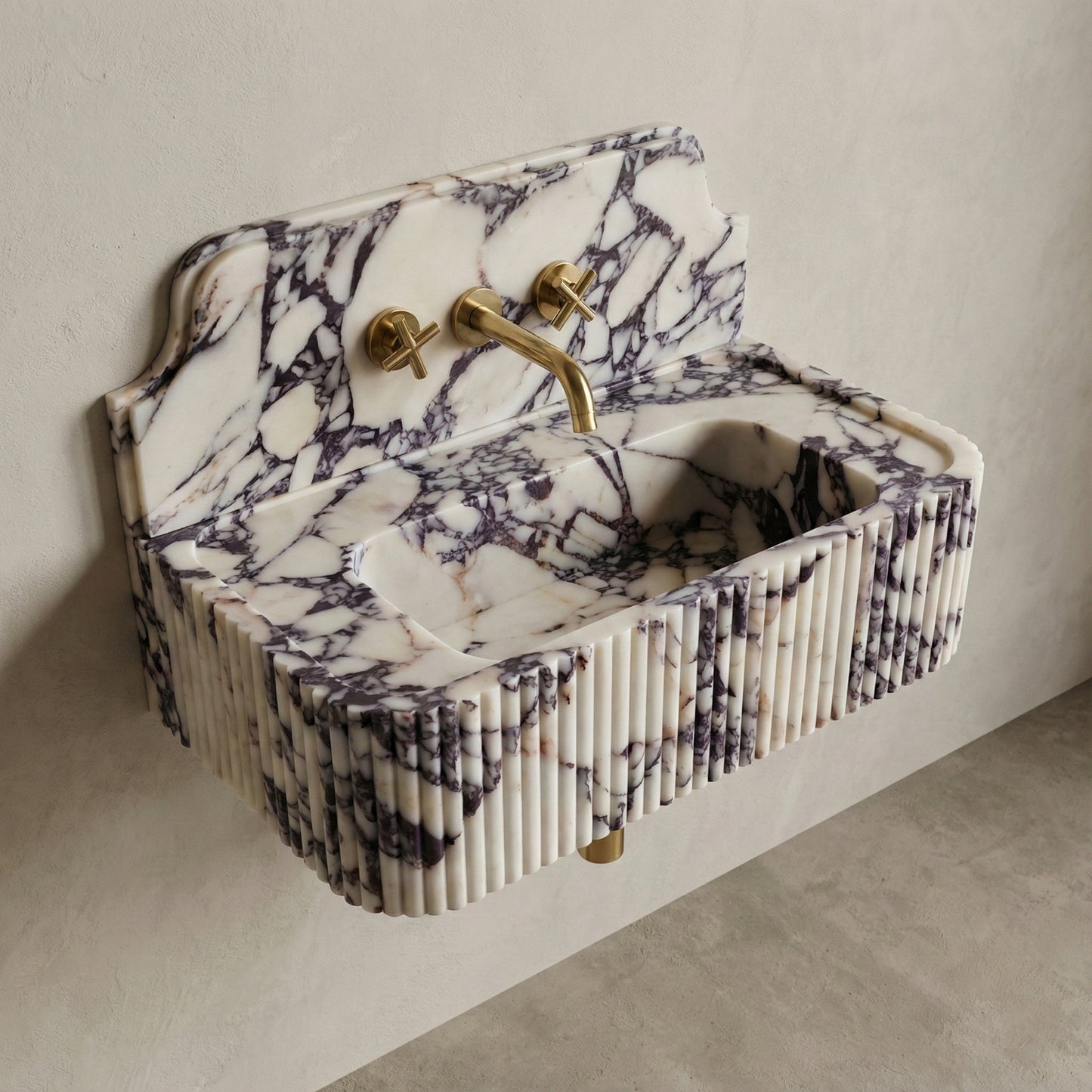 High-angle side view of a vintage-inspired Calacatta Viola marble sink, featuring a curved stone backsplash, fluted apron, and brass cross-handle faucet.
