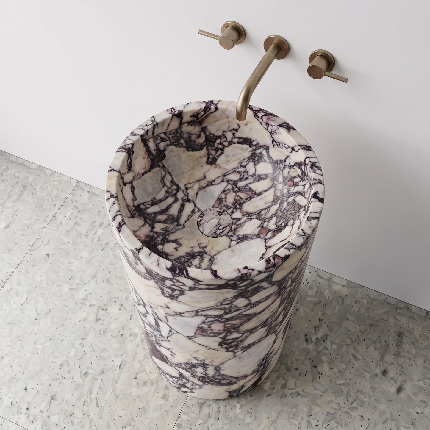 High-angle top view of a solid Calacatta Viola cylindrical pedestal sink highlighting deep purple brecciated veining and matching carved marble drain cover.