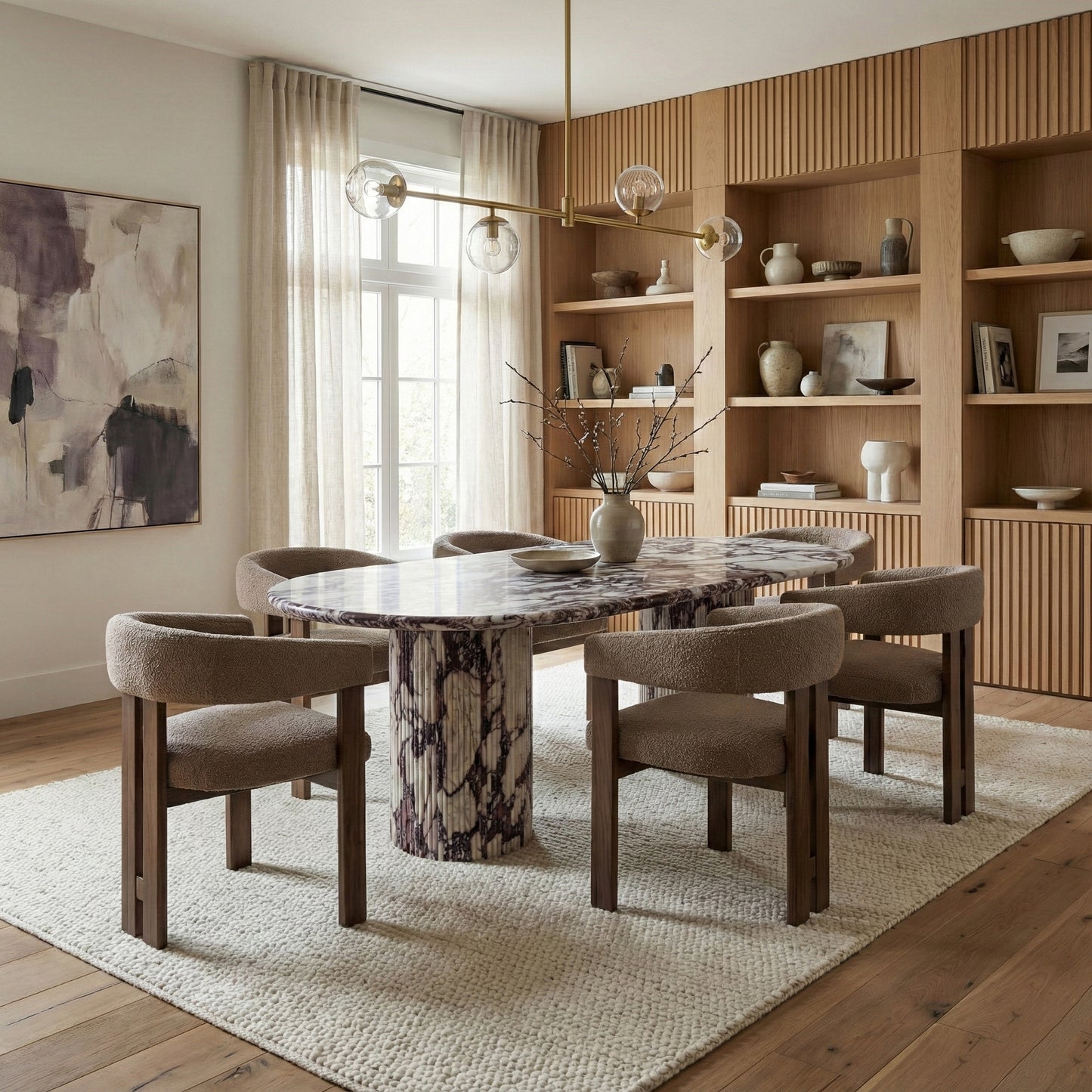 Modern dining room featuring a statement Calacatta Viola marble oval table, paired with upholstered armchairs, light wood shelving, and a brass linear chandelier.