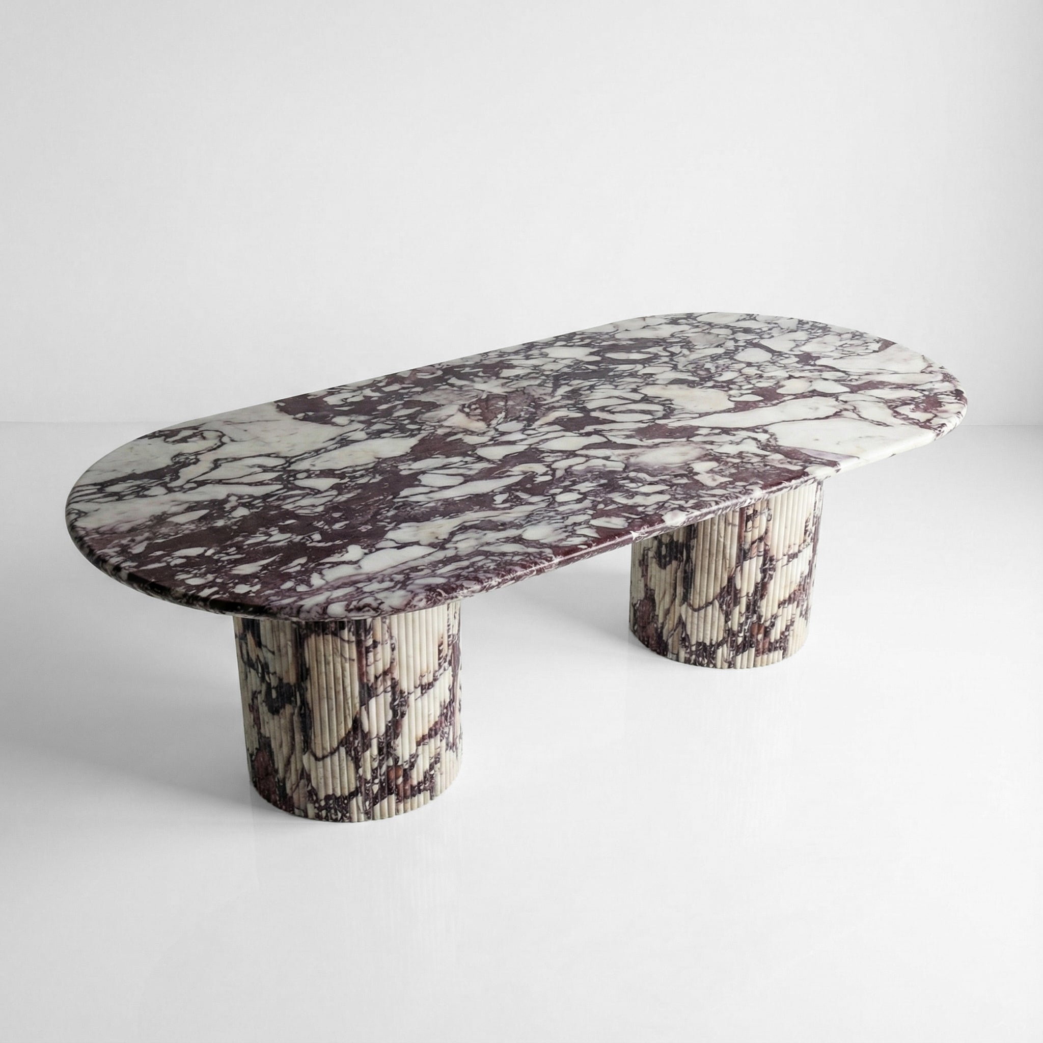 High-angle view of a luxury Calacatta Viola marble dining table featuring a large oval top and dual fluted pedestal bases with deep purple veining.
