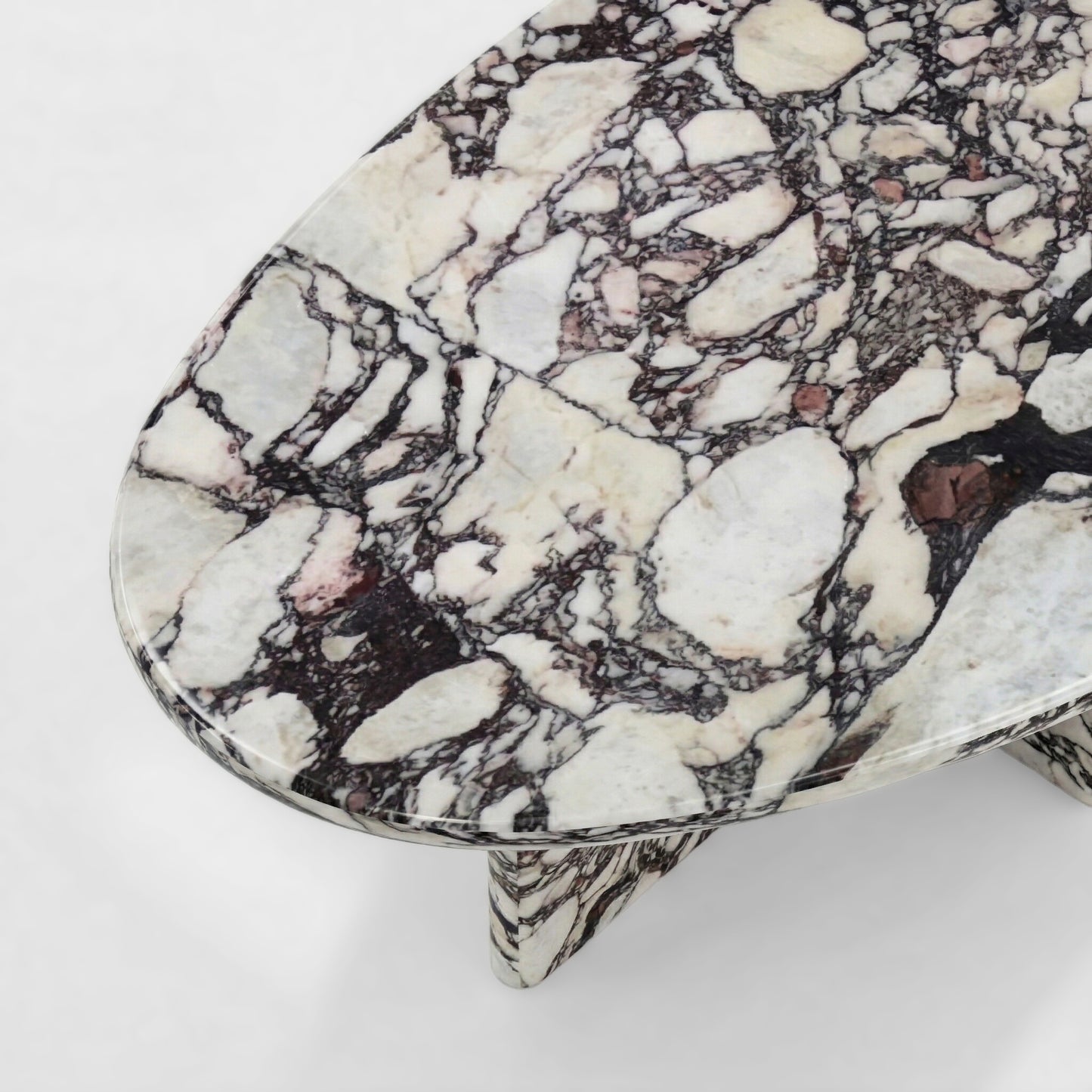 Side profile of a luxury Calacatta Viola marble coffee table featuring a sculptural pedestal base and an organic pebble-shaped top against a minimalist white background.