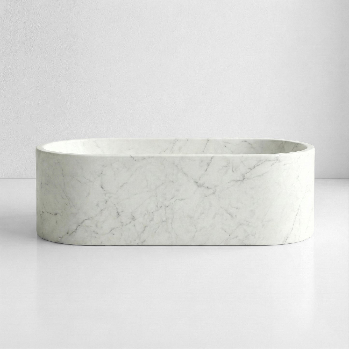 Front view of a minimalist oval bathtub carved from Italian Carrara marble, distinct for its understated elegance and fine grain pattern.