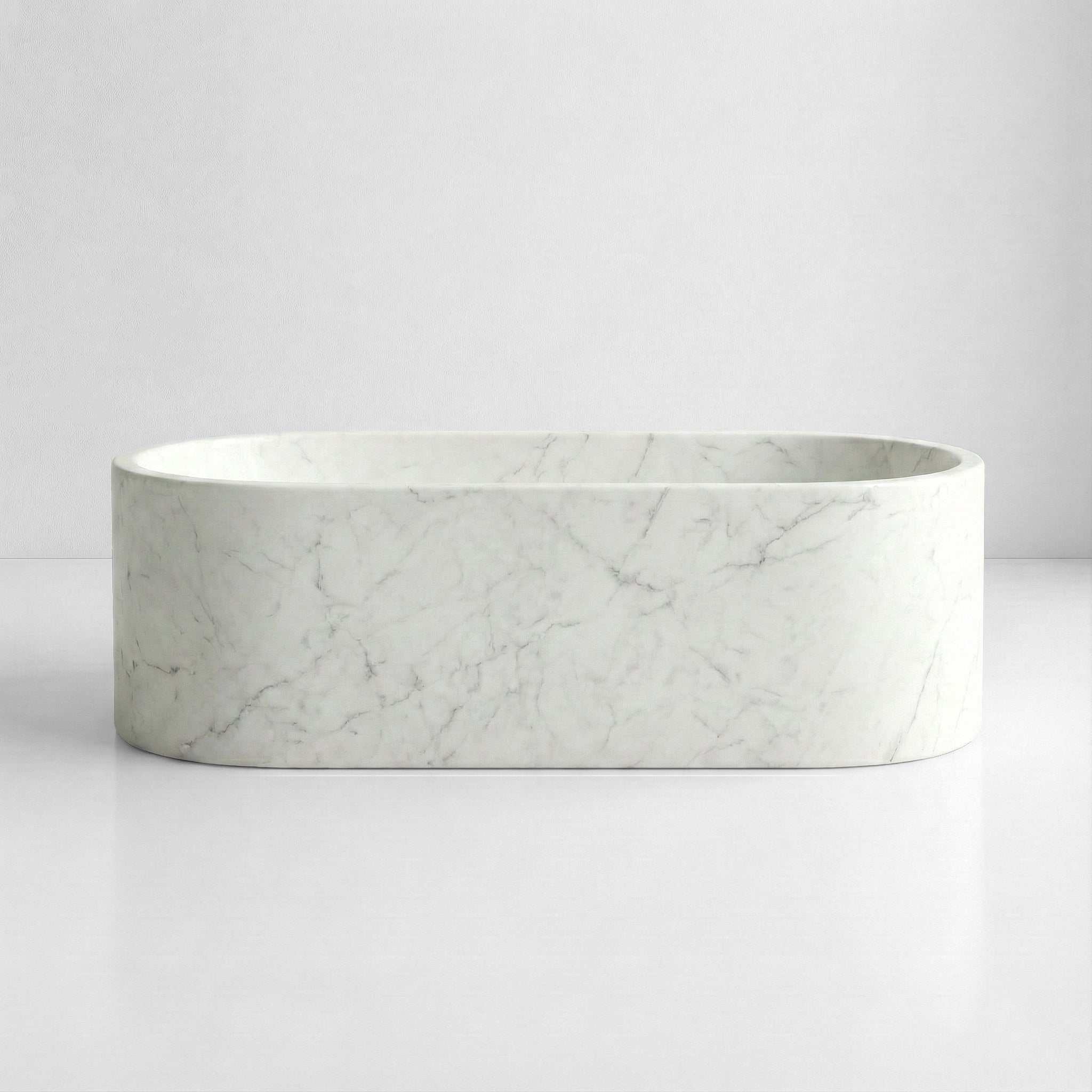 Front view of a minimalist oval bathtub carved from Italian Carrara marble, distinct for its understated elegance and fine grain pattern.