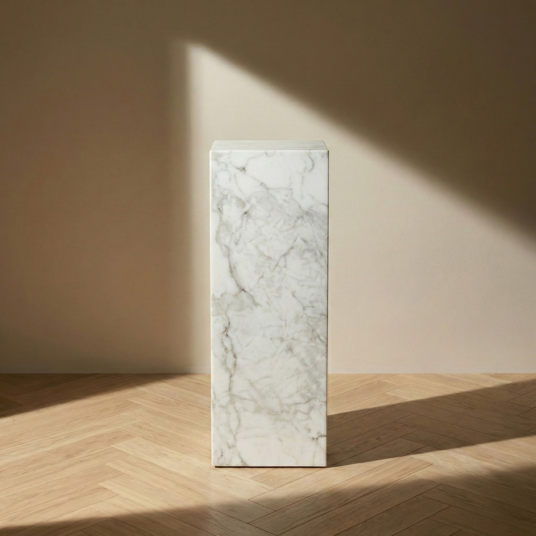 A front-on view of a Carrara marble pedestal stand against a neutral beige wall, showcasing the classic white and gray feathered veining and elegant vertical proportions.