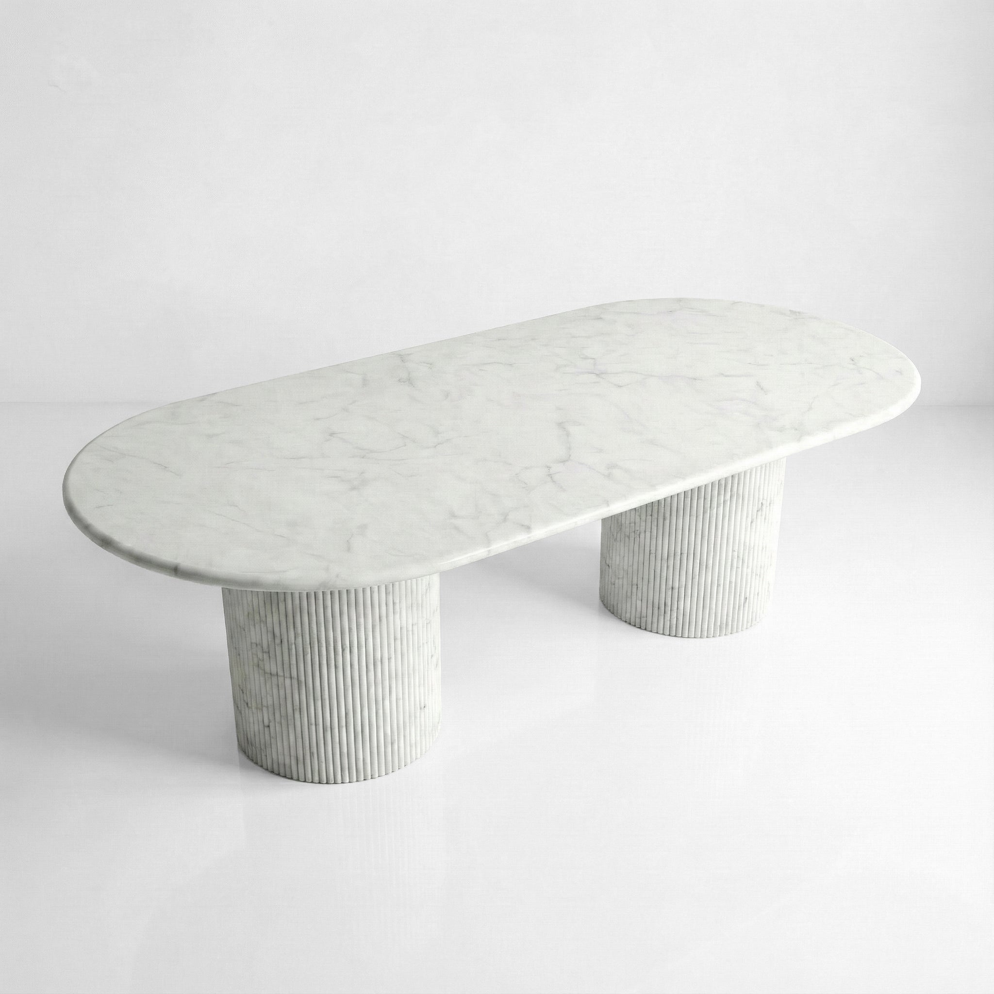 High-angle view of a large oval Carrara marble dining table, highlighting the clean white background and delicate grey mineral patterns.