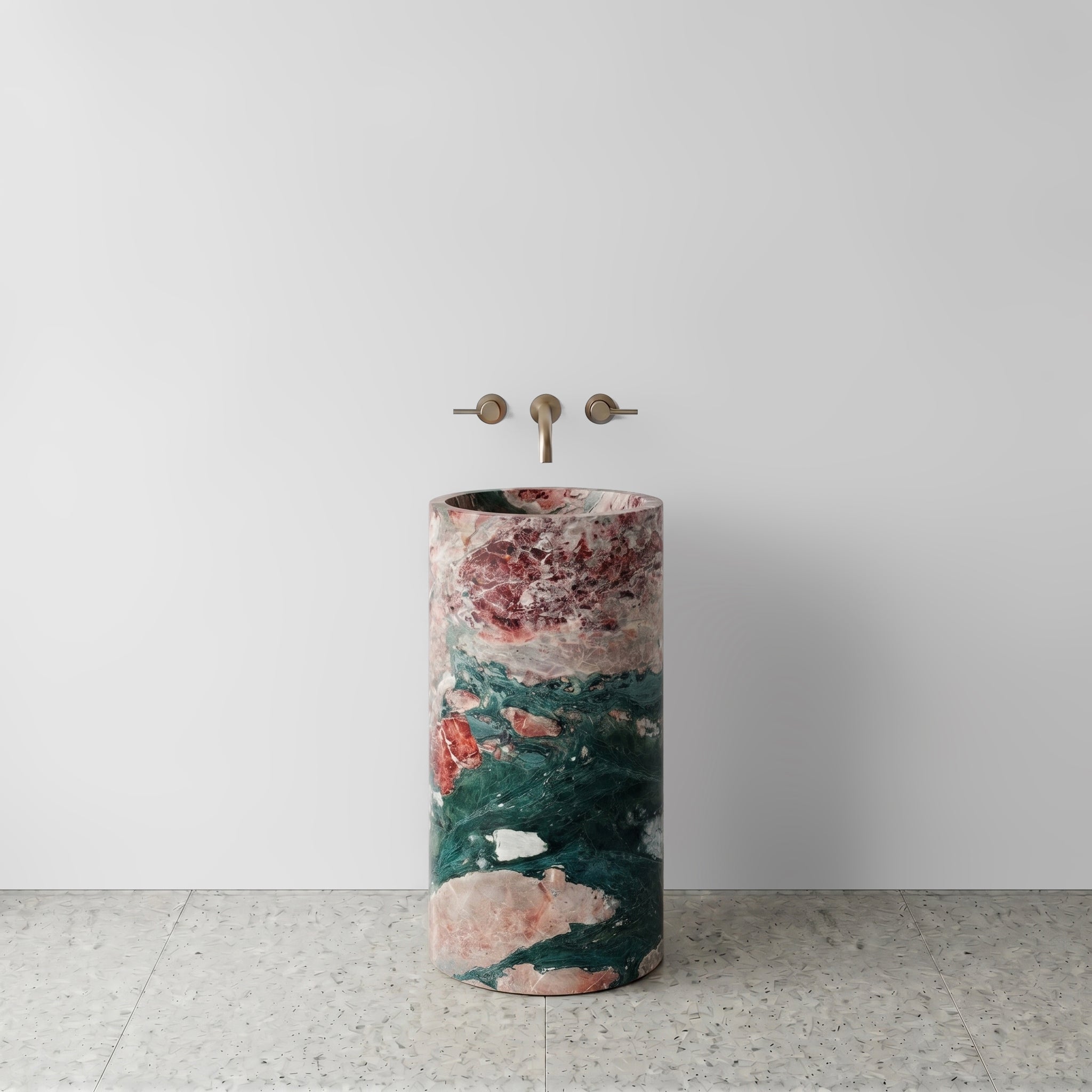 Front view of a monolithic Four Seasons marble cylinder pedestal sink featuring deep green and rose breccia veining with wall-mounted bronze tapware.