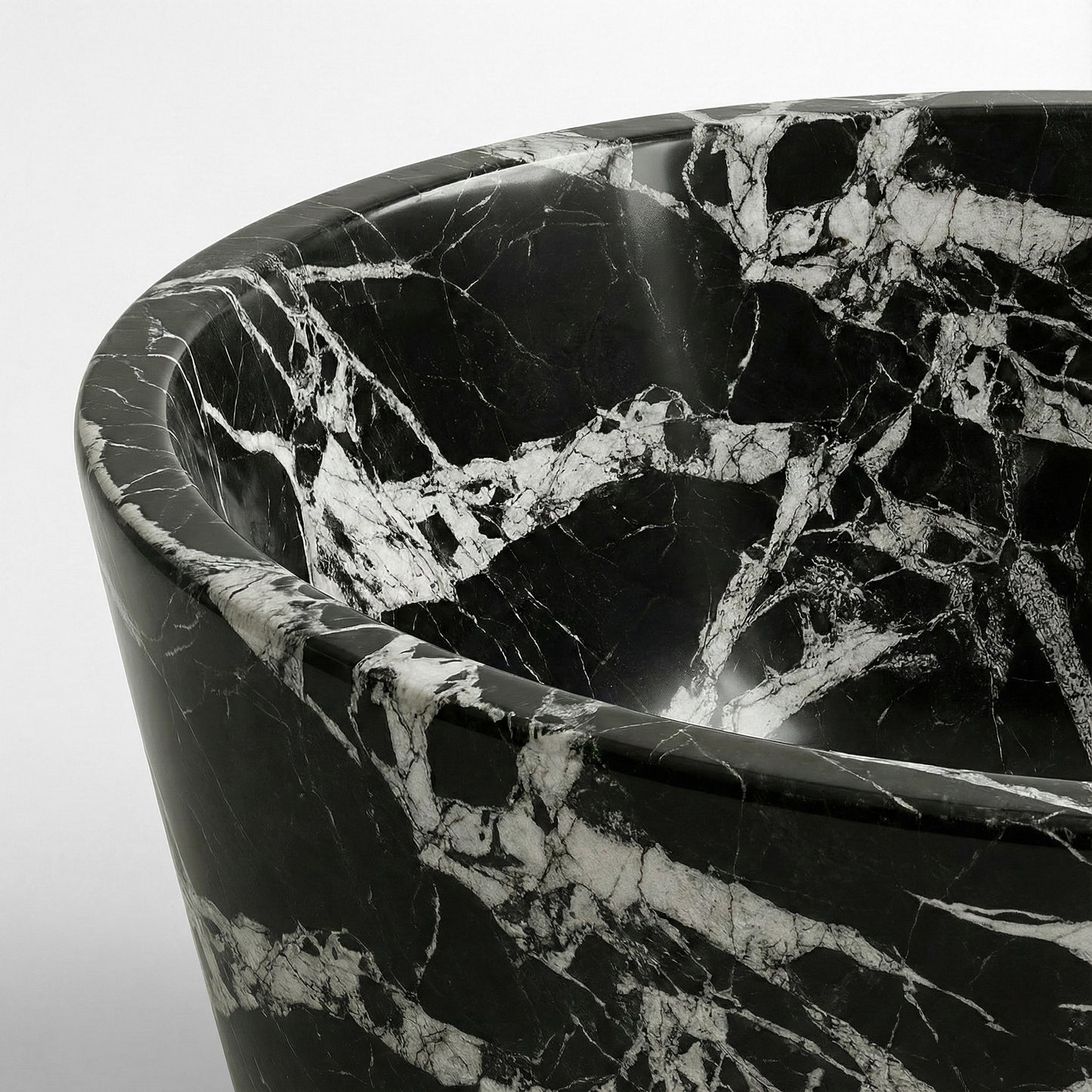 Close-up detail of a Grand Antique marble bathtub rim featuring a dramatic high-contrast pattern of large white brecciated fragments against deep black stone.