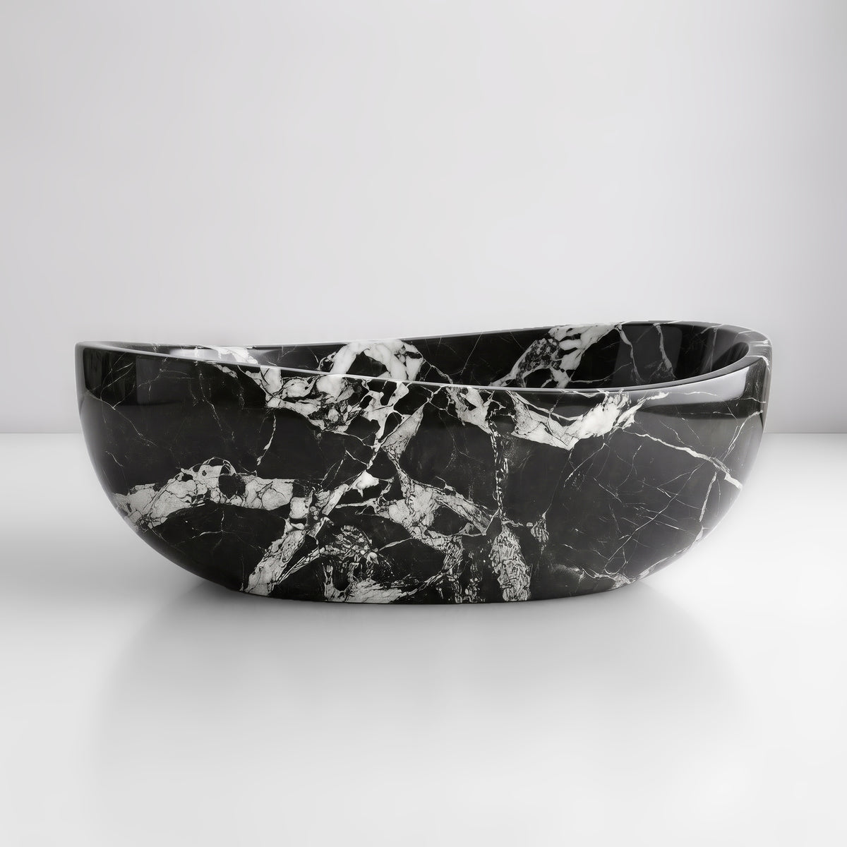 Front studio view of the freestanding Grand Antique marble wave bathtub, showcasing the organic dipping rim silhouette and high-contrast monochrome breccia veining across the deep black polished stone exterior.