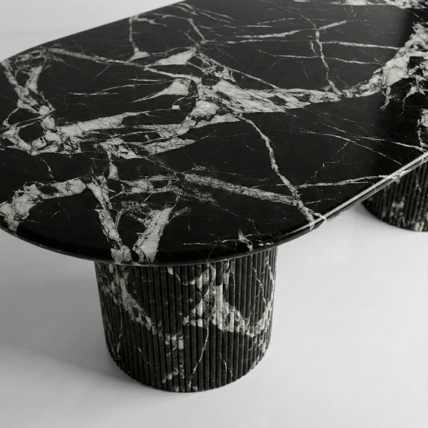 Close-up side profile of a Grand Antique marble dining table, highlighting the high-contrast black and white stone pattern and fluted pedestal base.
