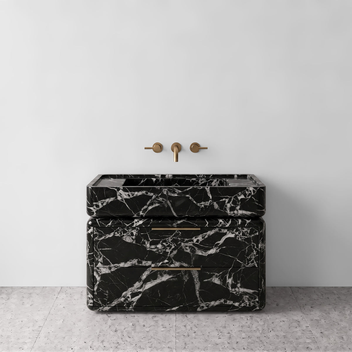 Front studio view of the freestanding Grand Antique marble double-drawer vanity, showcasing curved corners, dramatic high-contrast black-and-white breccia veining, an integrated trough basin, and horizontal brushed brass pulls paired with wall-mounted brass tapware set against a white wall and terrazzo flooring.