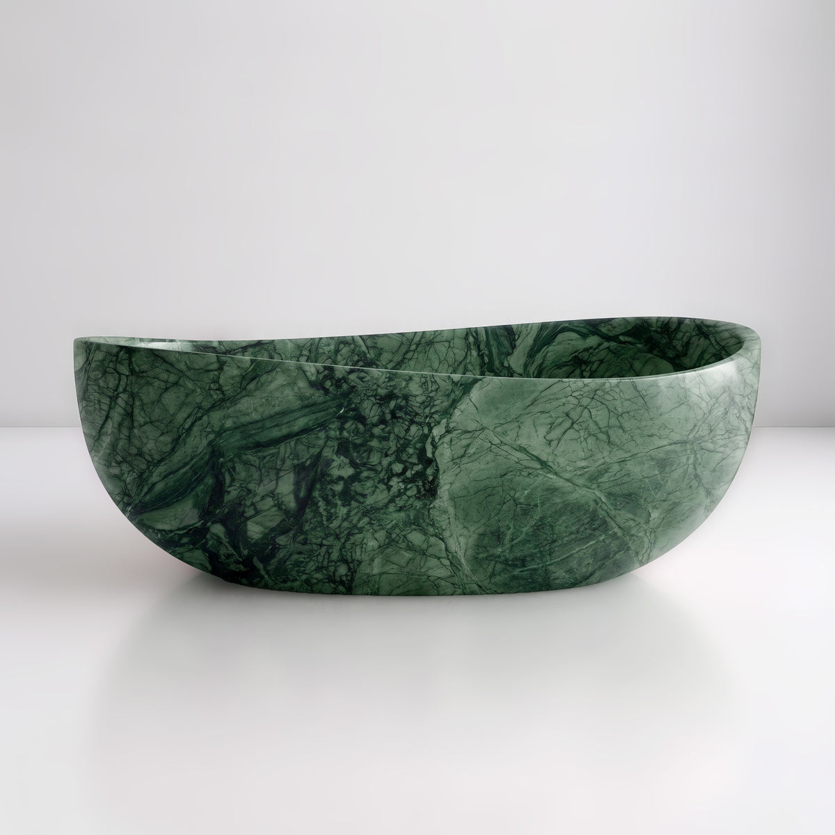 Front studio view of the freestanding Green Guatemala marble wave bathtub, showcasing the organic dipping rim silhouette and deep emerald-green field with dark webbed veining across the polished stone exterior.