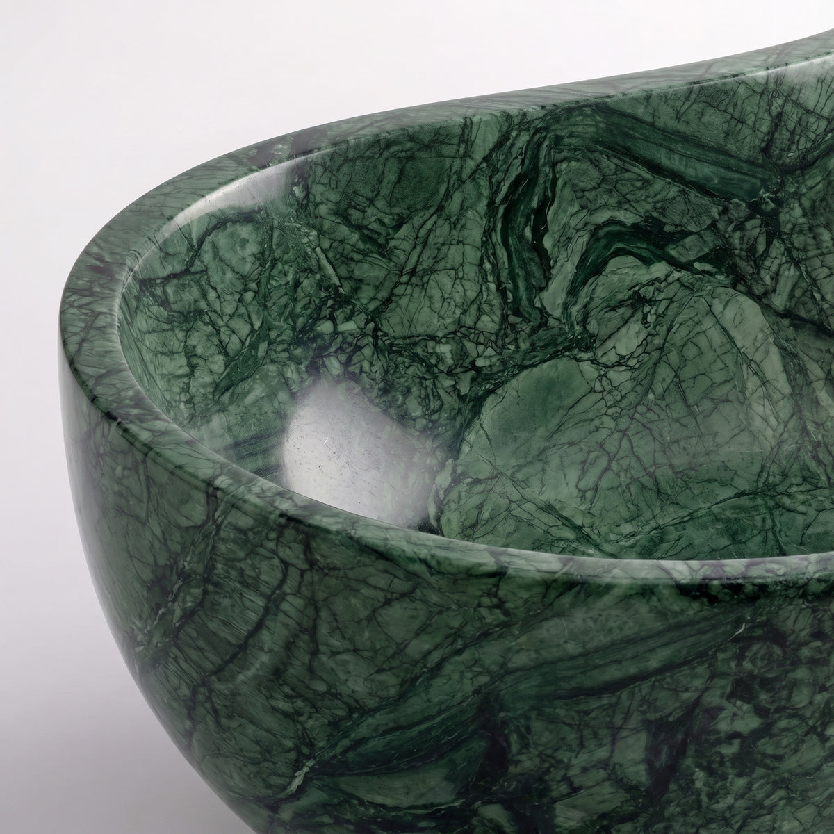 Close-up overhead detail shot of the Green Guatemala marble wave bathtub rim, displaying the hand-finished curve, polished surface, and intricate webbed charcoal veining across rich green stone.
