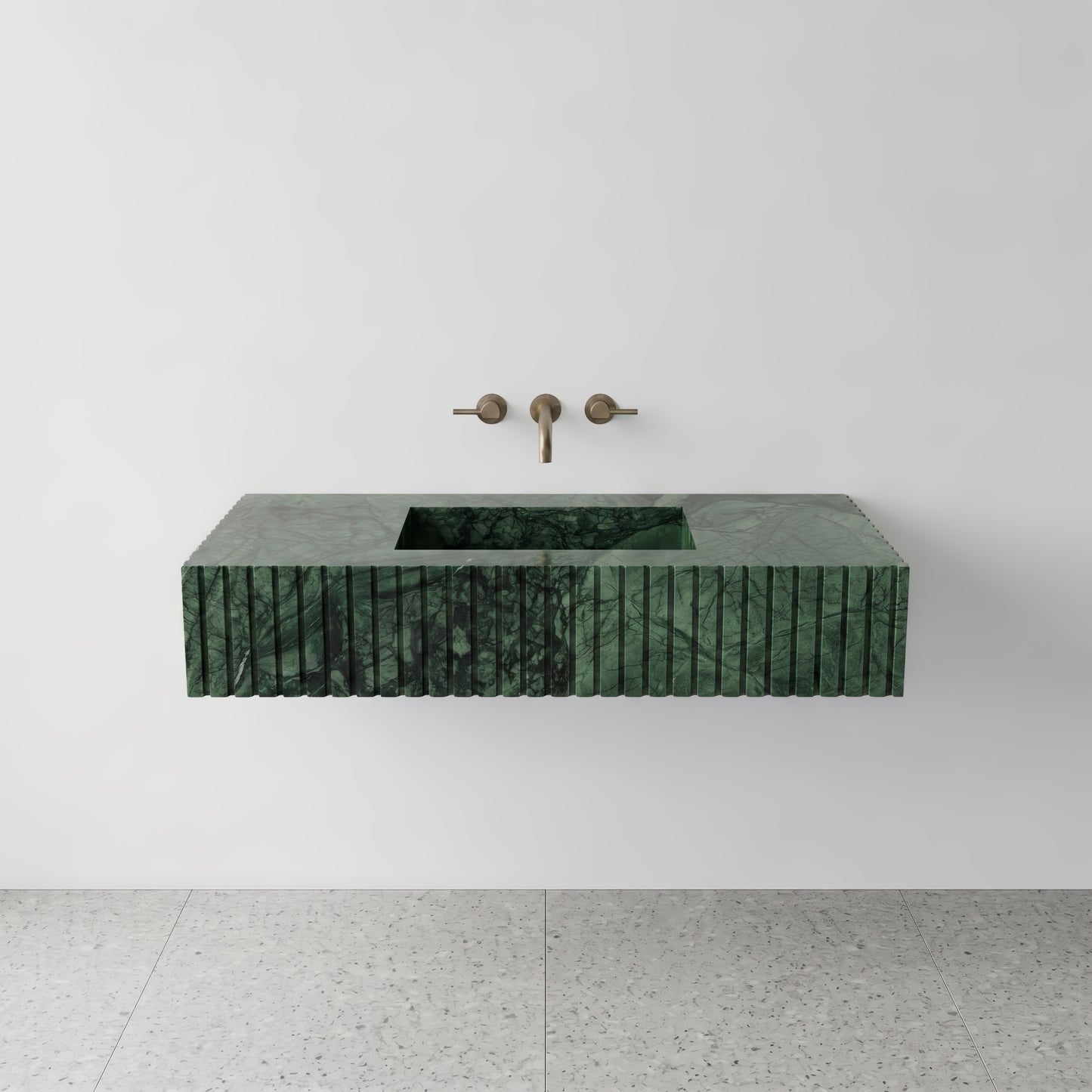 Front studio view of a luxury floating single sink vanity made of Verde Guatemala green marble, featuring an architectural fluted apron front design and a wall-mounted brushed bronze faucet.