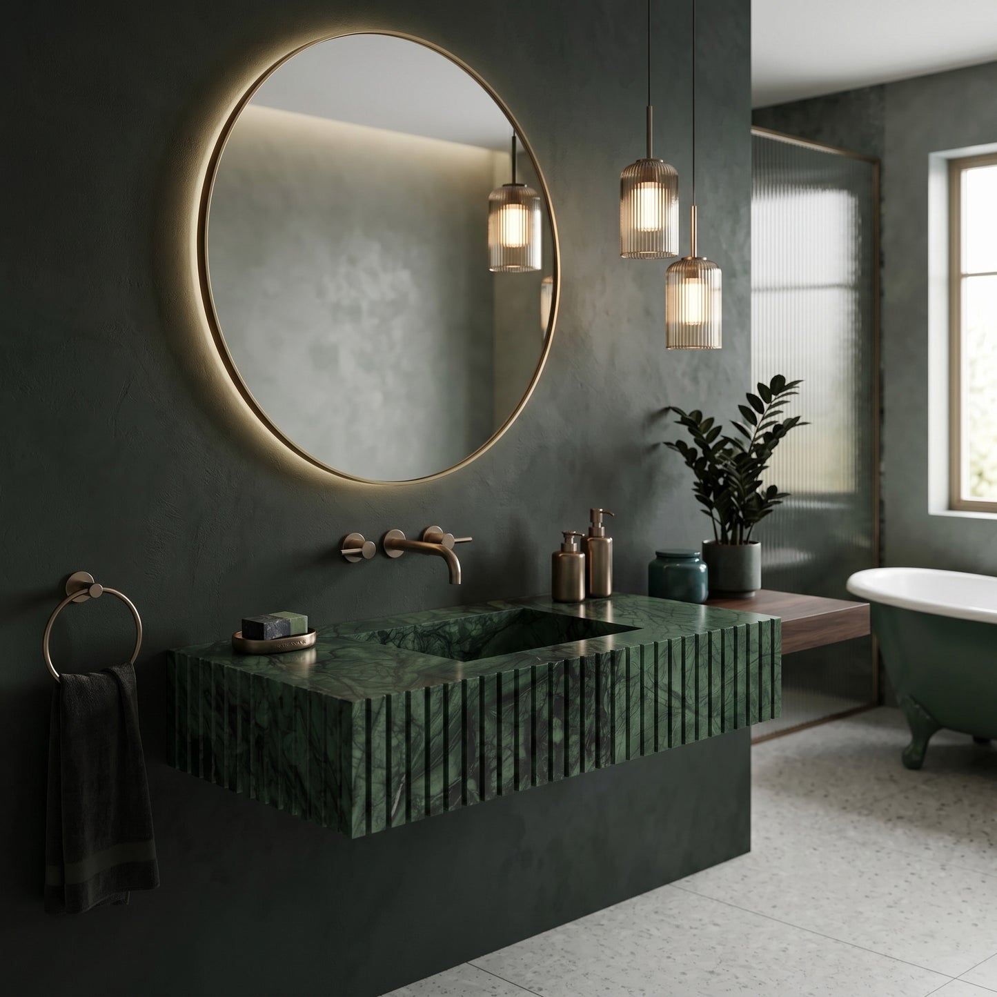 Moody dark green bathroom interior featuring a fluted green marble single sink, a large round backlit mirror, fluted glass pendant lights, a floating wood ledge, and a matching green clawfoot bathtub.