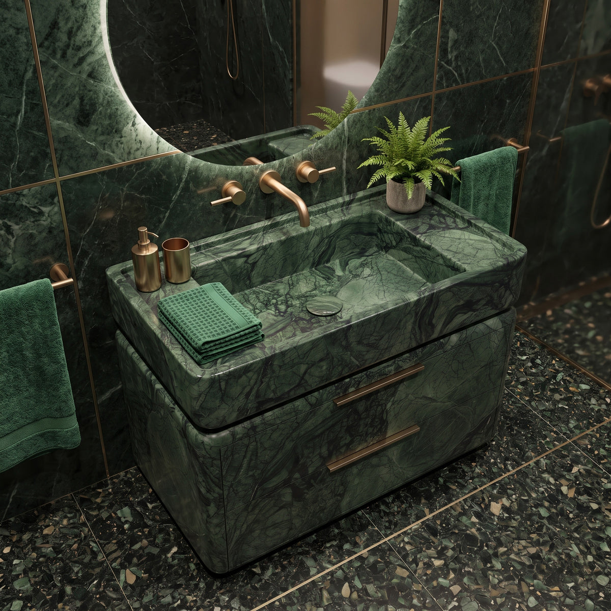 Luxurious emerald green bathroom interior featuring the curved Green Guatemala marble double-drawer vanity, wall-mounted brushed brass tapware, a large round backlit mirror, matching green marble slab walls with brass inlay, dark terrazzo flooring, and plush green bath towels.