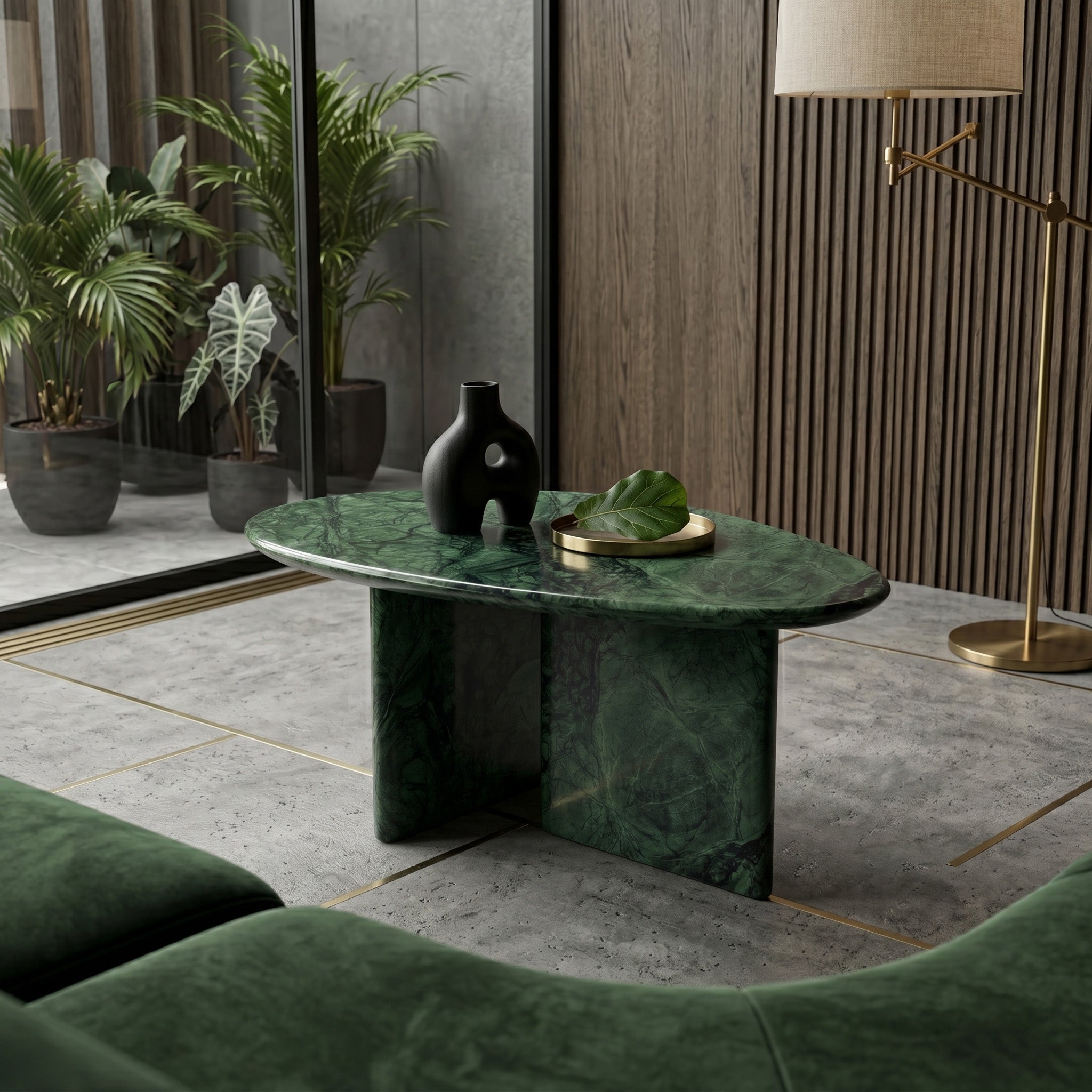 Contemporary living room interior featuring a pebble-shaped Green Guatemala marble coffee table as a centerpiece, styled with a black vase and minimalist brass decor on a textured concrete floor.