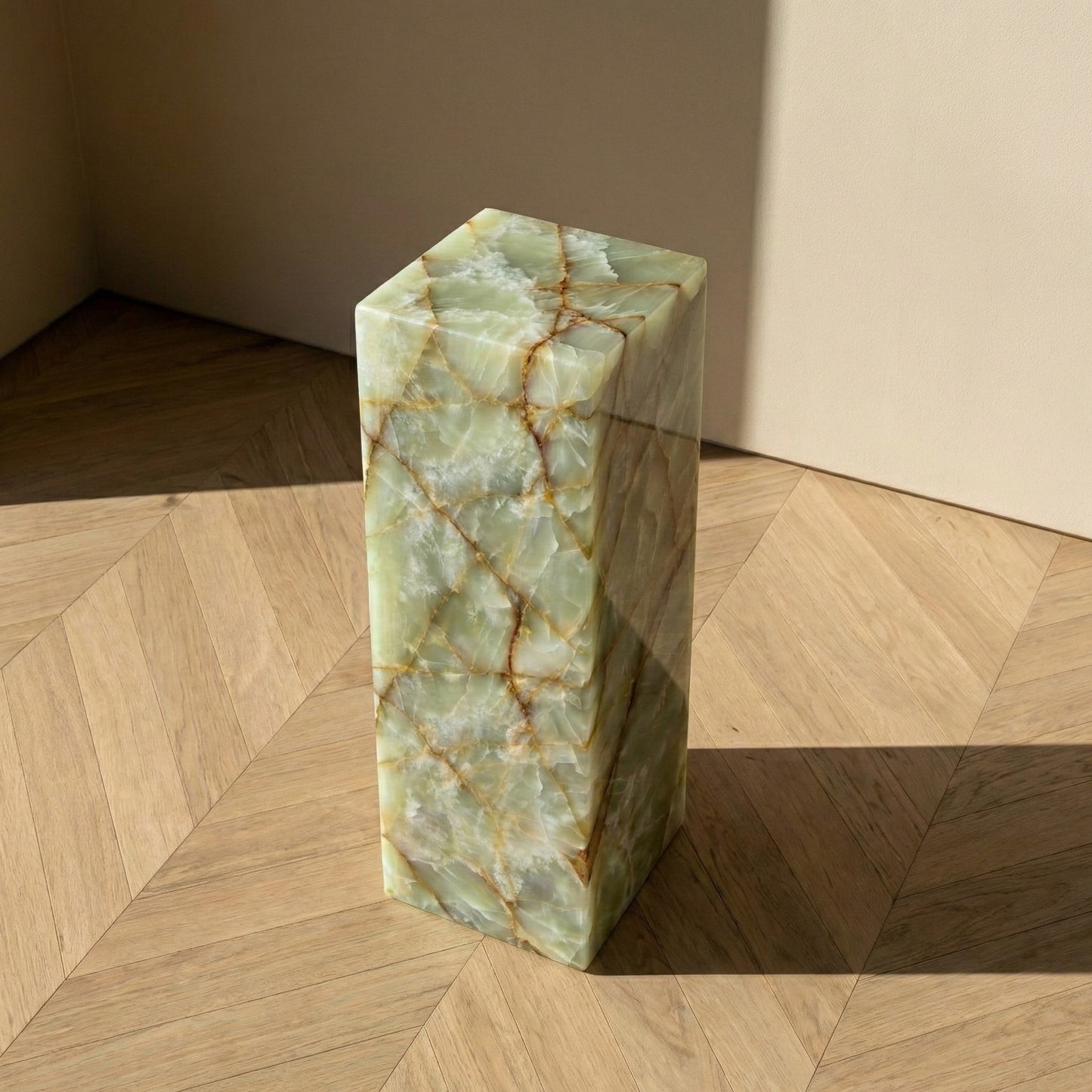 An angled overhead view of a rectangular Green Onyx plinth on a wood herringbone floor, highlighting its polished surface and the complex, web-like natural patterns.