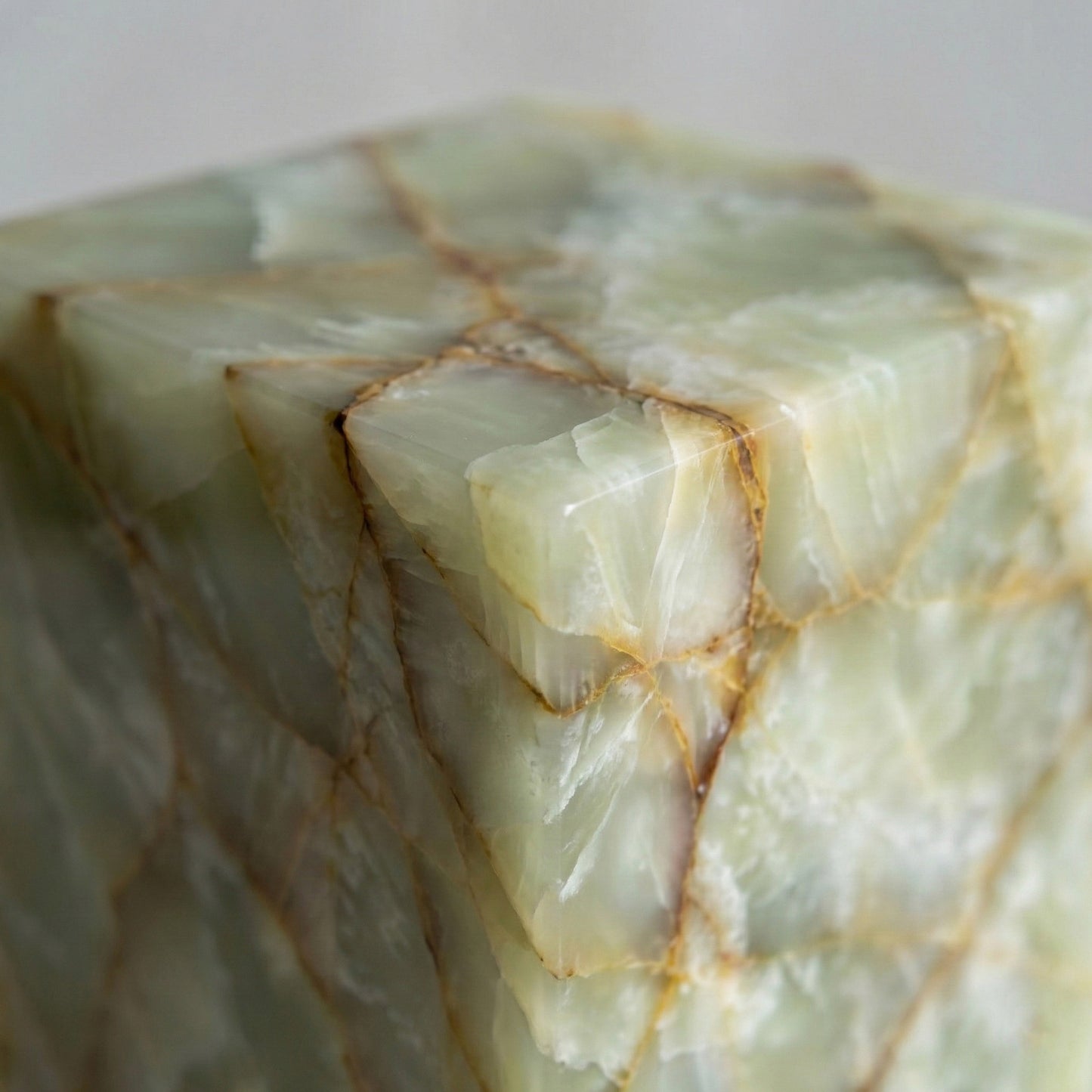 An extreme close-up of a Green Onyx pedestal corner, showcasing the translucent, jade-like crystalline structure and the dramatic rust-colored veining.
