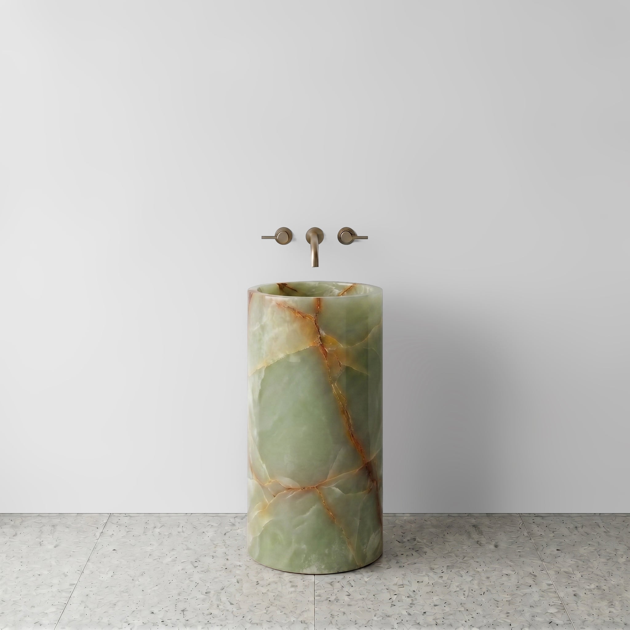 Front view of a solid Green Onyx cylinder pedestal sink featuring translucent jade tones and rust veining with wall-mounted bronze tapware.