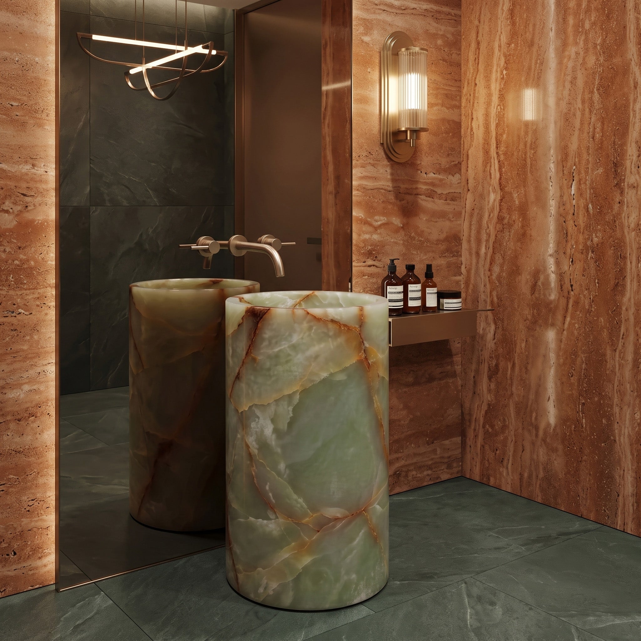 Freestanding Green Onyx round pedestal basin in a luxury powder room with warm red travertine walls, floor-to-ceiling mirror, and brass sconce.