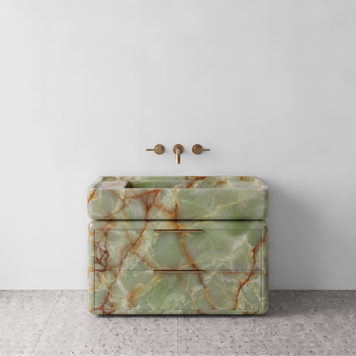 Front studio view of the freestanding Green Onyx double-drawer vanity, featuring rounded corners, an integrated trough basin, horizontal brushed brass pulls, and wall-mounted three-hole brass tapware set against a white wall and terrazzo flooring.