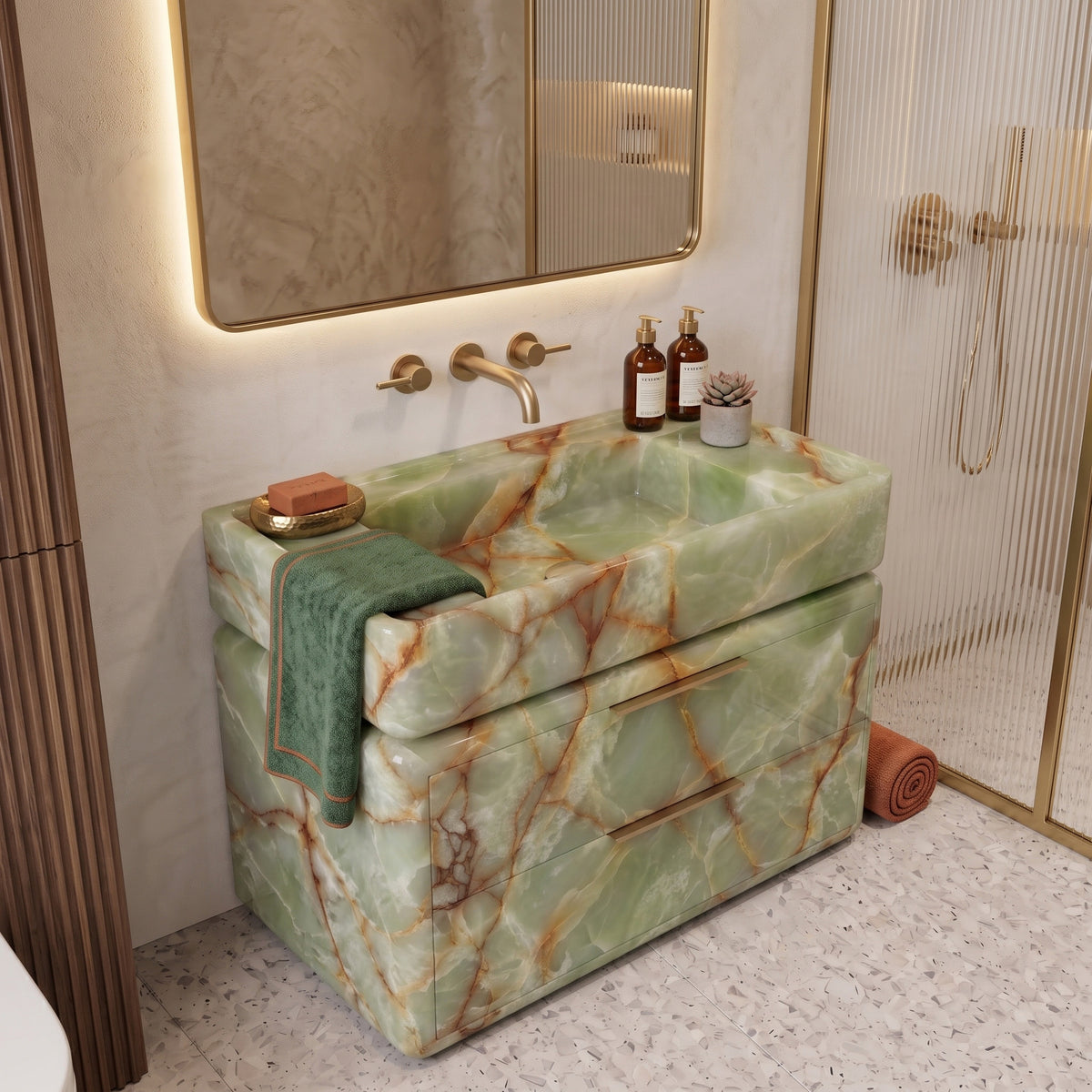 Luxury bathroom sanctuary featuring the curved Green Onyx double-drawer vanity draped with a green hand towel, wall-mounted brushed brass tapware, an illuminated backlit mirror, fluted wall accents, and a reeded-glass shower screen on terrazzo tile.