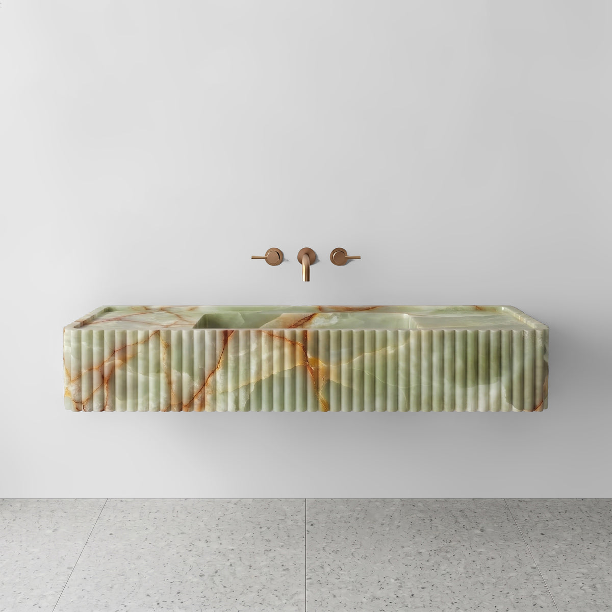 Front view of the Green Onyx fluted monolith sink showing translucent jade tones and rust-colored mineral veining across the vertical convex ribbed apron and wall-mounted brushed bronze faucet.
