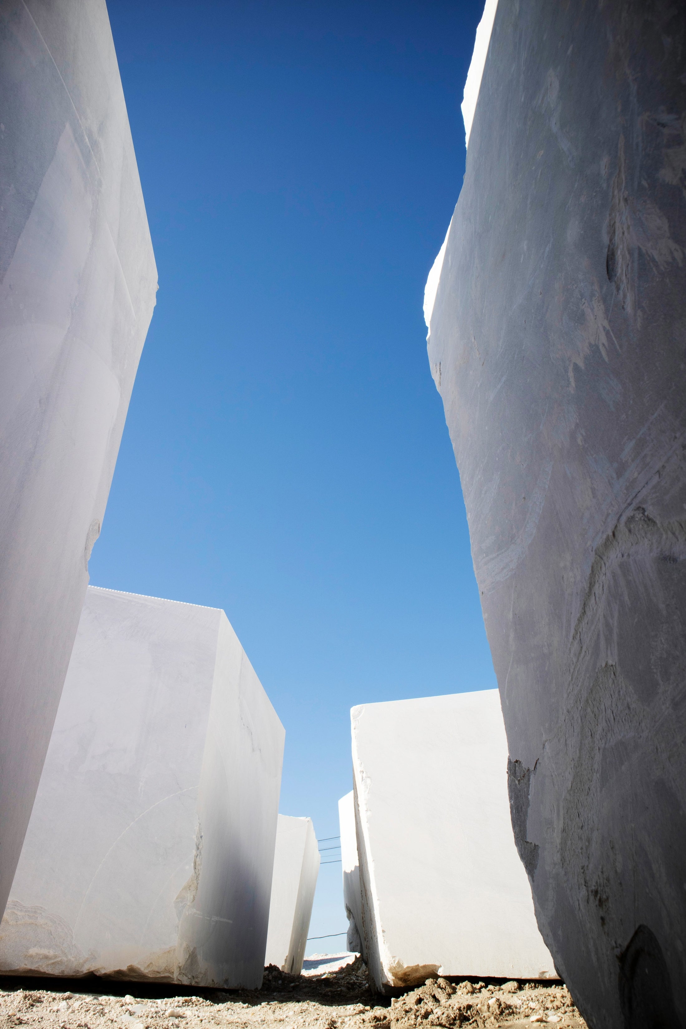 Monumental raw white marble blocks standing in the quarry under a blue sky, representing the premium sourcing of natural stone for bespoke bathtubs, sinks, tables, and custom furniture.
