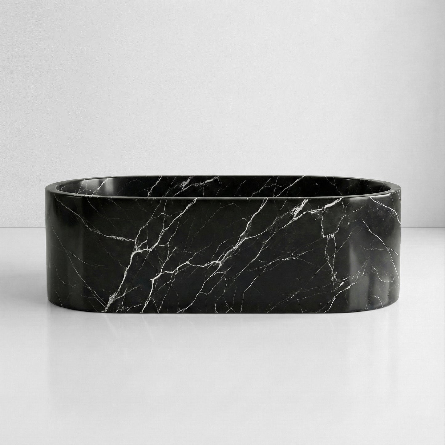 Front elevation of a freestanding oval bathtub carved from Nero Marquina marble, displaying a high-contrast black and white natural stone pattern.