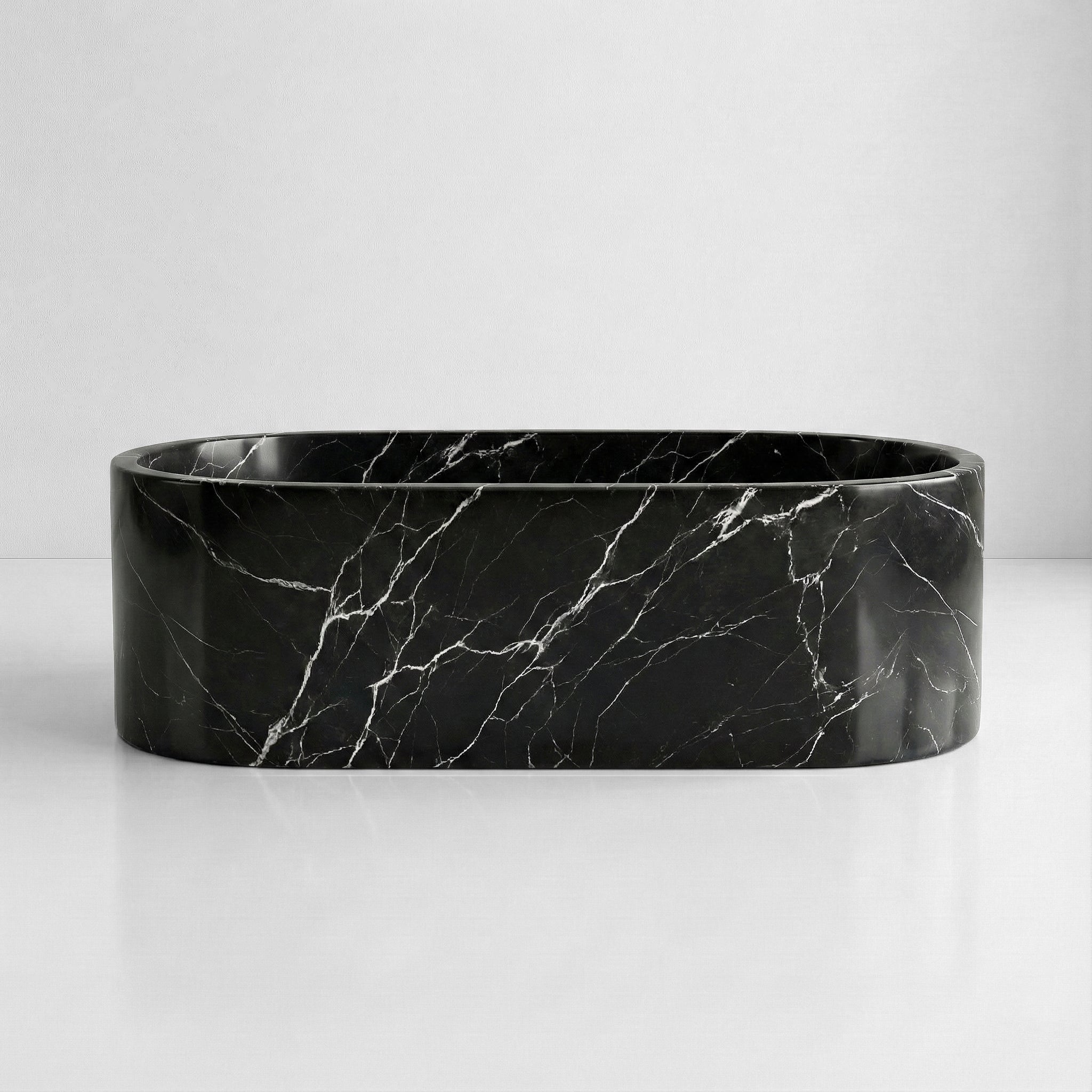 Front elevation of a freestanding oval bathtub carved from Nero Marquina marble, displaying a high-contrast black and white natural stone pattern.