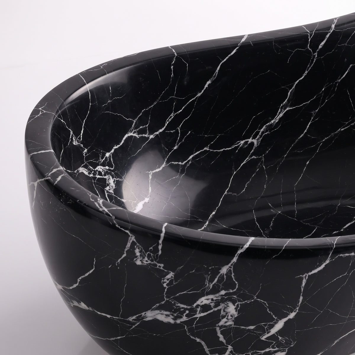 Close-up overhead detail shot of the Nero Marquina marble wave bathtub rim, displaying the hand-finished curve, polished stone texture, and sharp contrast of fine white lightning veins branching across pitch-black marble.