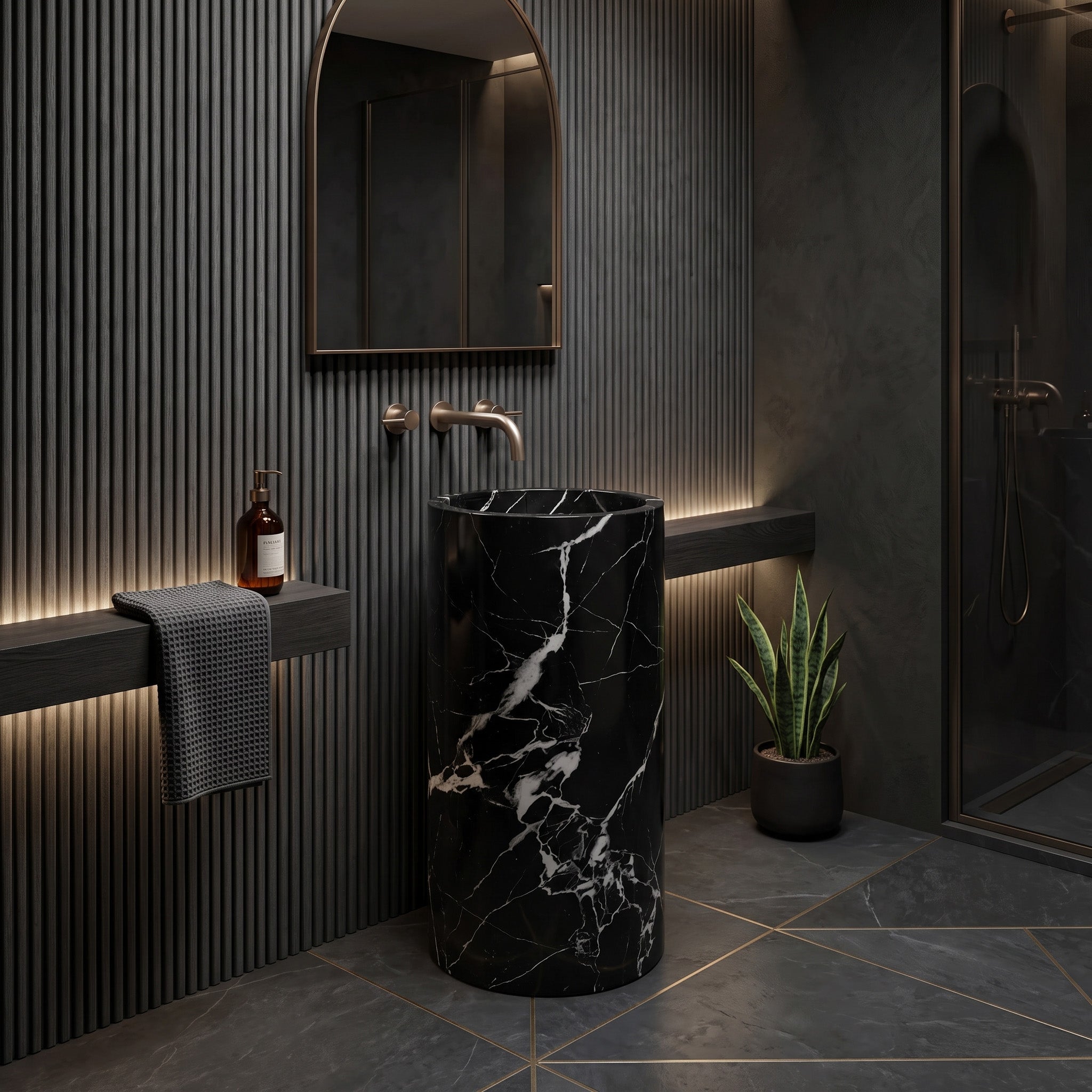 Freestanding Nero Marquina round marble pedestal sink in a moody modern bathroom with charcoal fluted walls, bronze arch mirror, and backlit floating shelf.