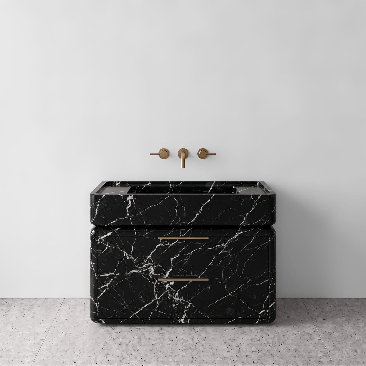 Front studio view of the freestanding Nero Marquina marble double-drawer vanity, featuring rounded corners, an integrated trough basin, horizontal brushed brass pulls, and wall-mounted three-hole brass tapware set against a white wall and terrazzo flooring.