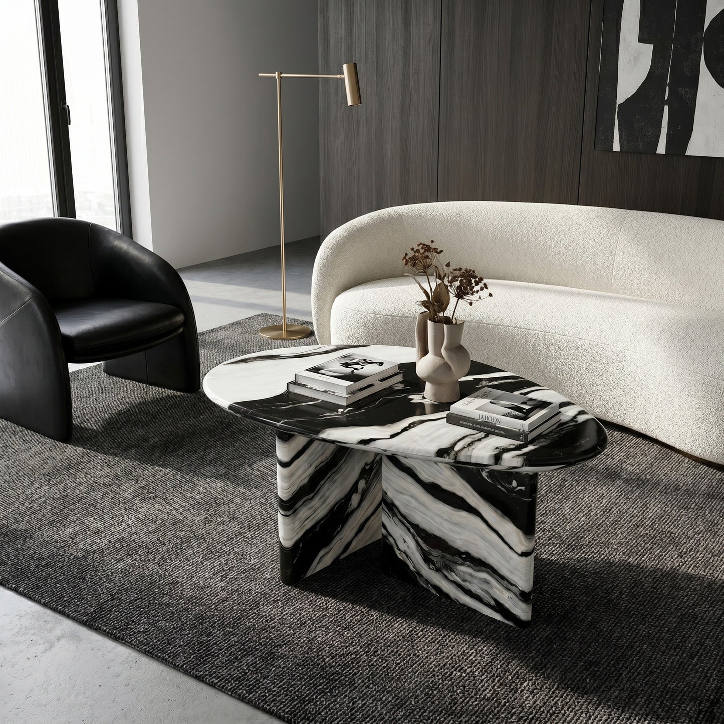 Modern living room interior showcasing a bespoke pebble-shaped Panda White marble coffee table as a functional centerpiece, styled on a dark textured rug alongside a curved white sofa.