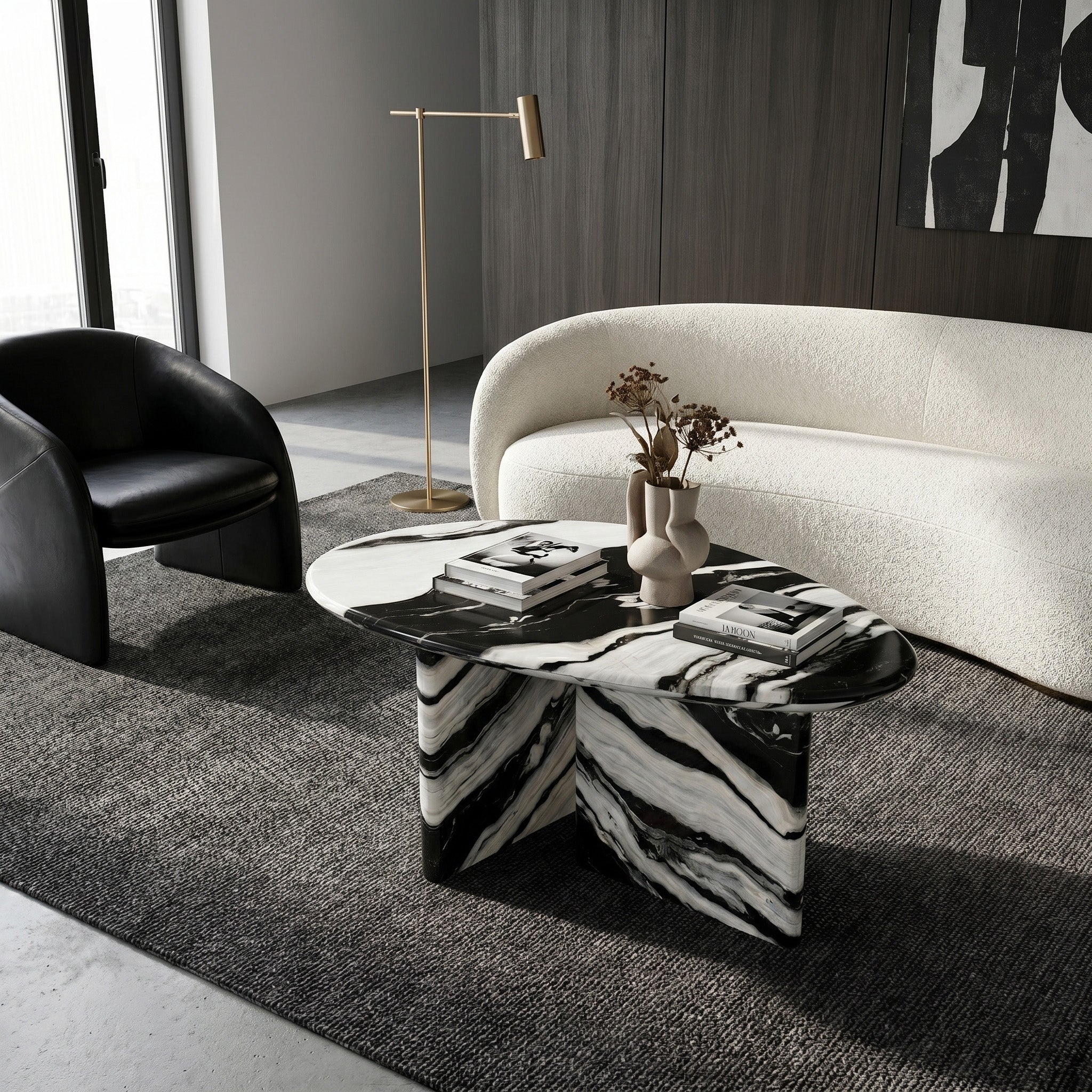 Modern living room interior showcasing a bespoke pebble-shaped Panda White marble coffee table as a functional centerpiece, styled on a dark textured rug alongside a curved white sofa.