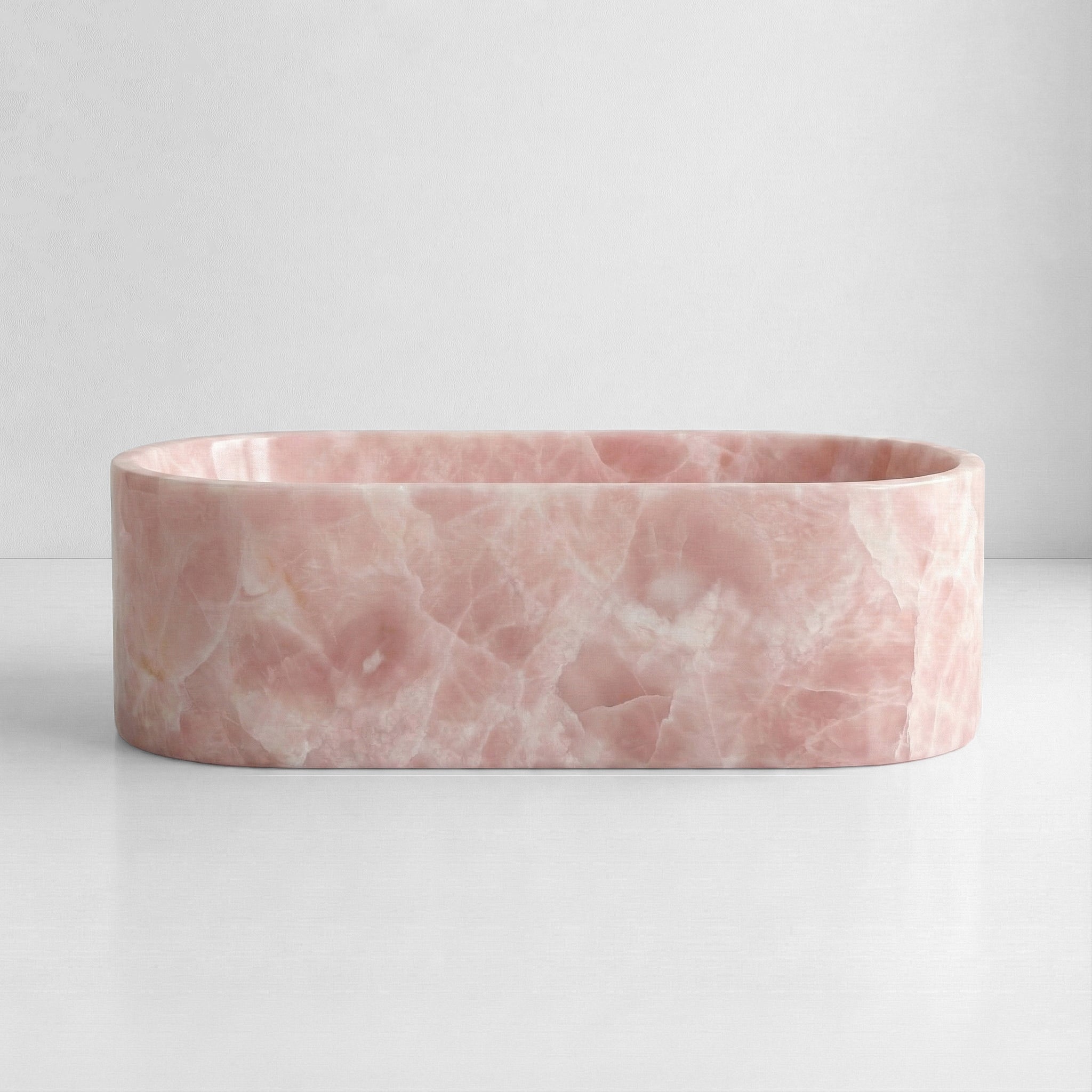 Front elevation of a luxury freestanding Pink Onyx bathtub displaying translucent pastel pink tones and natural stone variations.