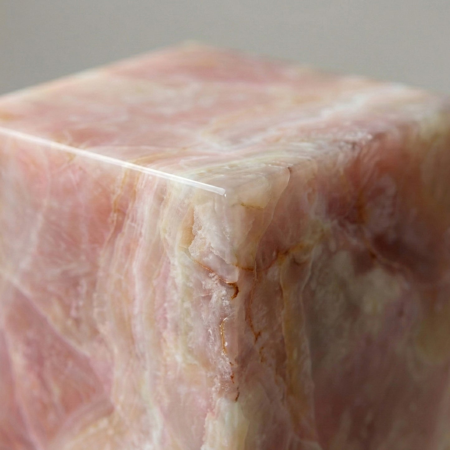An extreme close-up of a Pink Onyx pedestal corner, showcasing the translucent, crystalline layers of pastel pink and the precision-mitered edge.