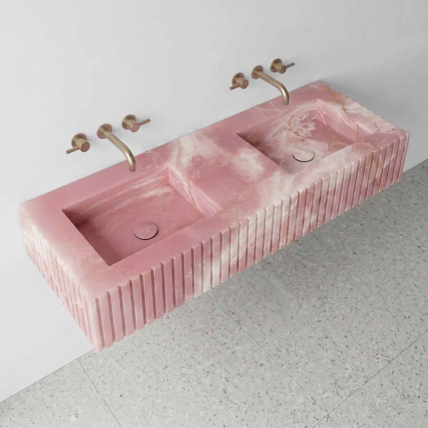 High-angle view of a wall-mounted Pink Onyx gemstone sink featuring dual integrated basins and a custom fluted stone apron.