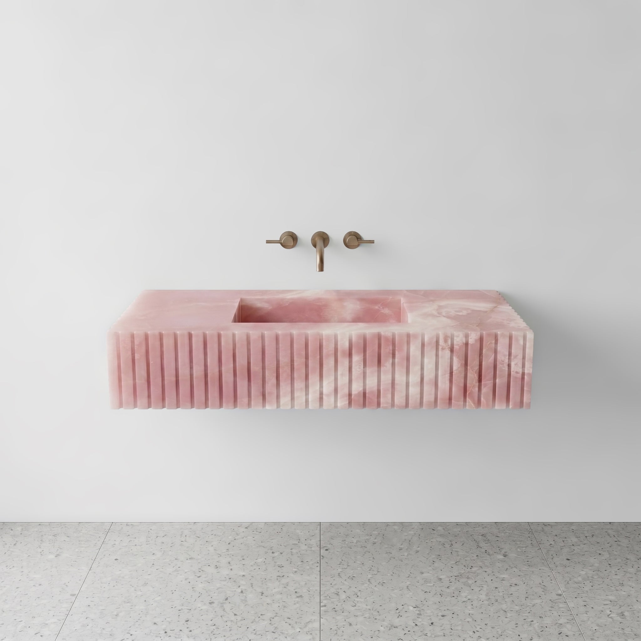 Front studio view of a luxury floating single sink vanity made of translucent Pink Onyx, featuring an architectural fluted apron front design and a wall-mounted brushed bronze faucet.
