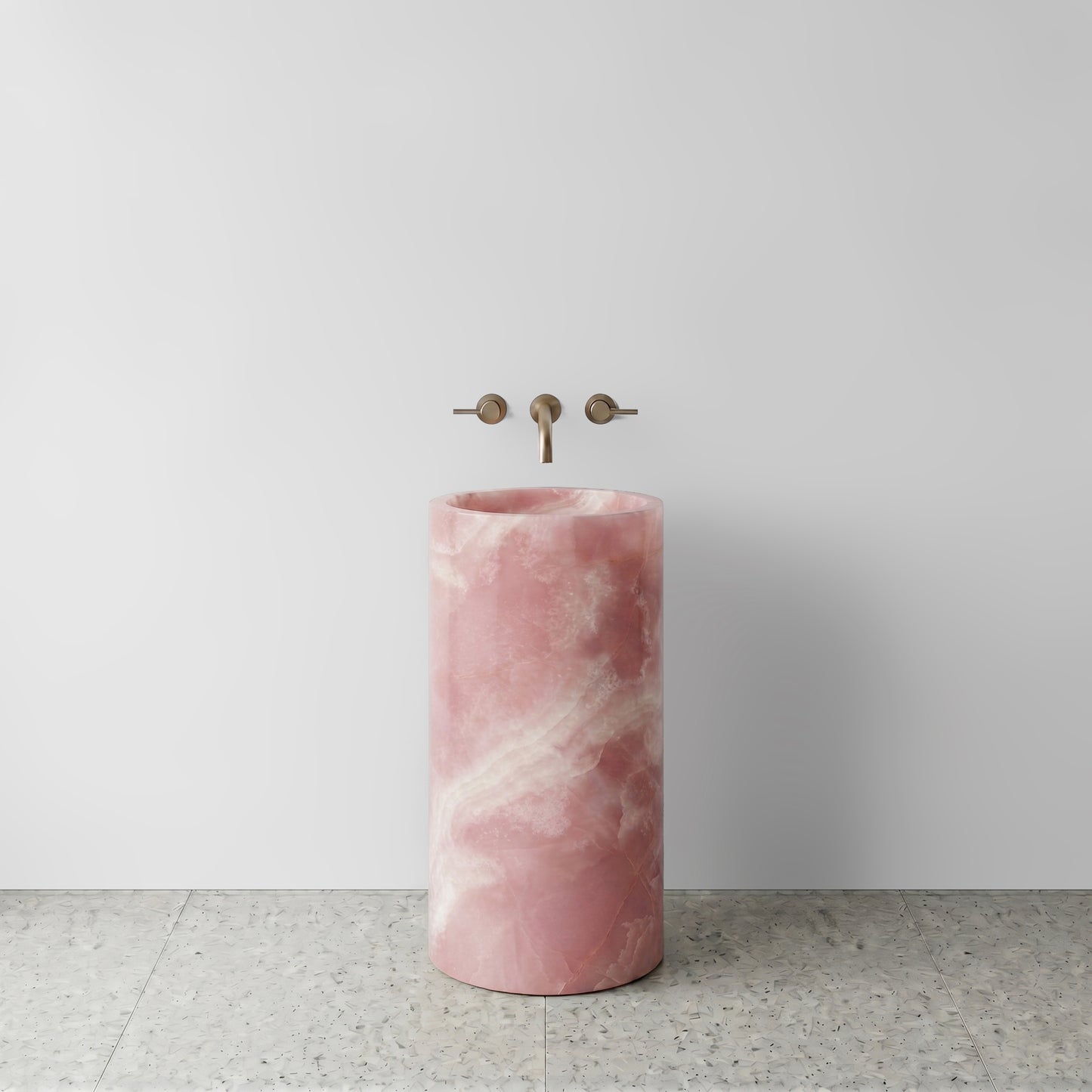 Front view of a solid Pink Onyx cylinder pedestal sink featuring luminous blush tones and white cloud veining with wall-mounted bronze tapware.