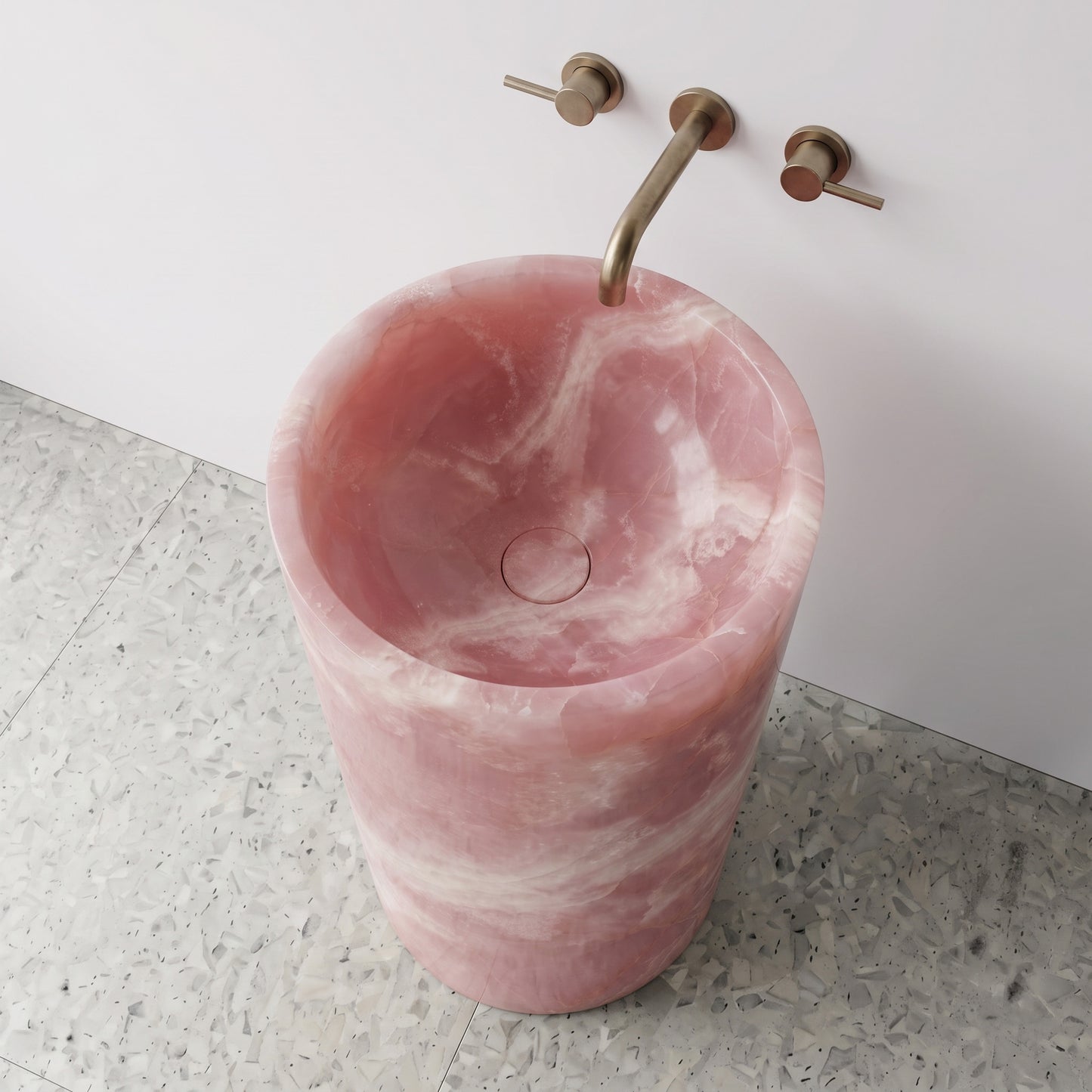 High-angle top view of a Pink Onyx cylindrical gemstone sink highlighting translucent rose layers and matching integrated carved stone drain cap.