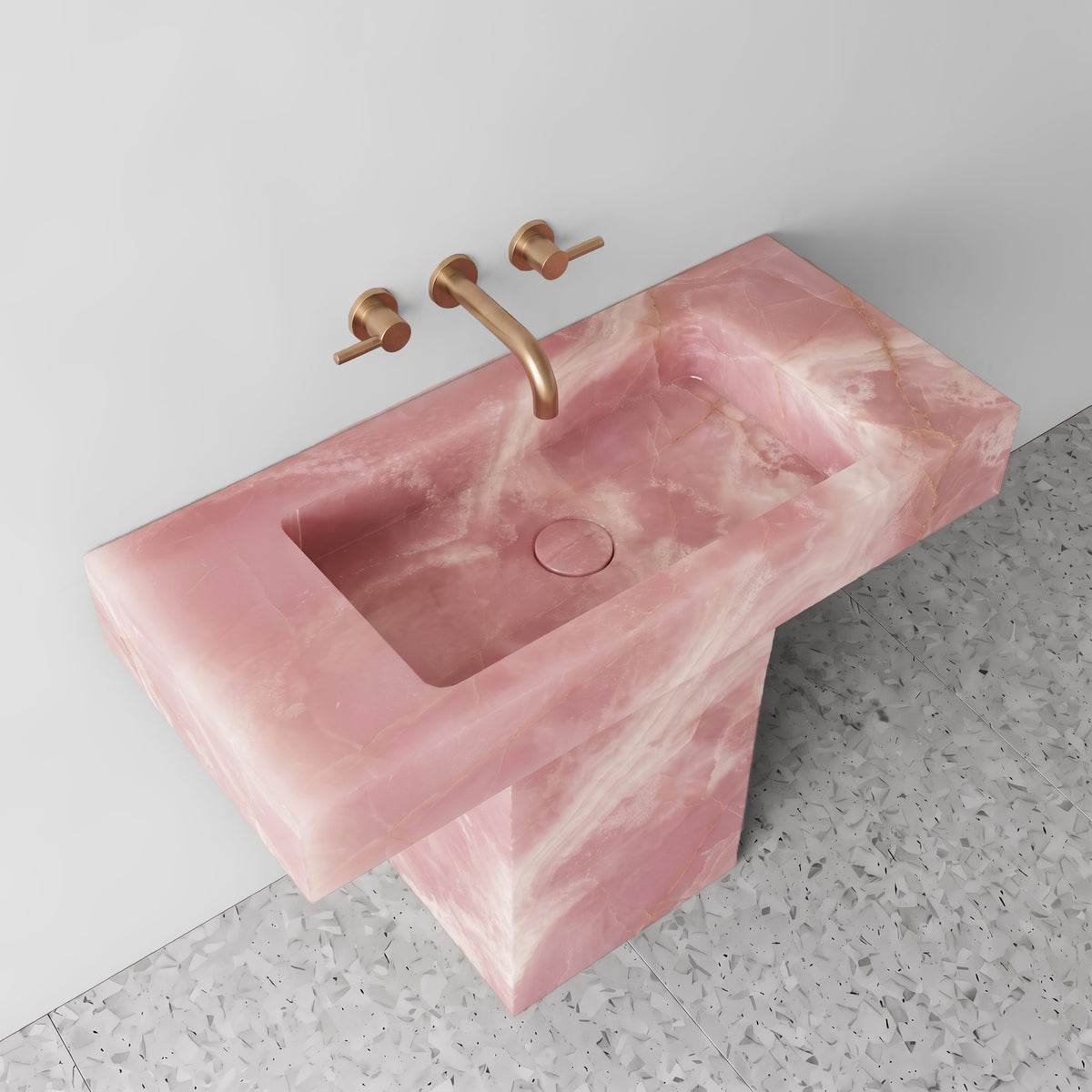 High-angle perspective highlighting the translucent pink gemstone trough, matching Pink Onyx drain cover, and brushed brass wall-mounted faucet.