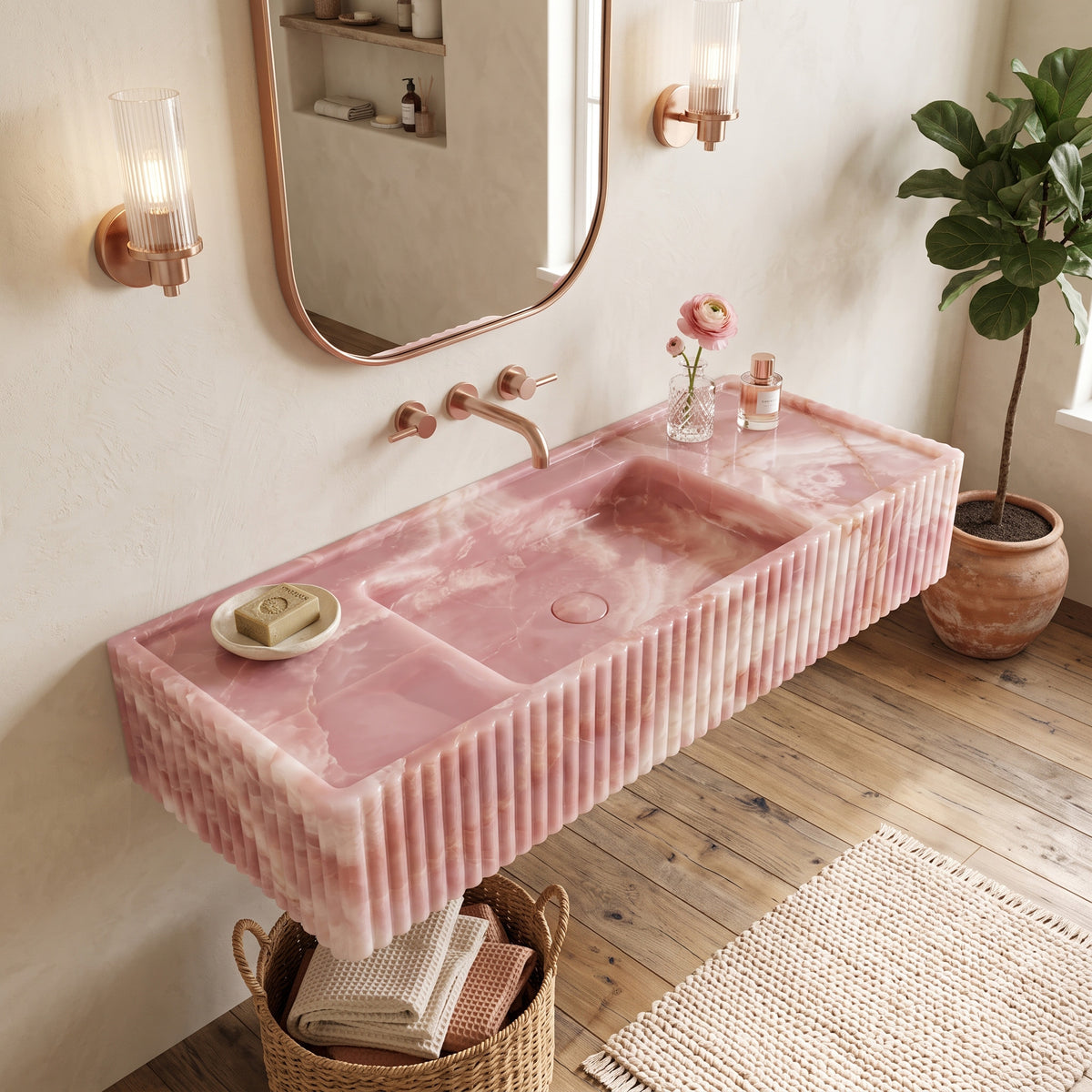 Bright, warm bohemian-luxe bathroom interior featuring the floating Pink Onyx fluted stone sink paired with a rounded bronze mirror, ribbed glass wall sconces, woven baskets, and natural timber floors.