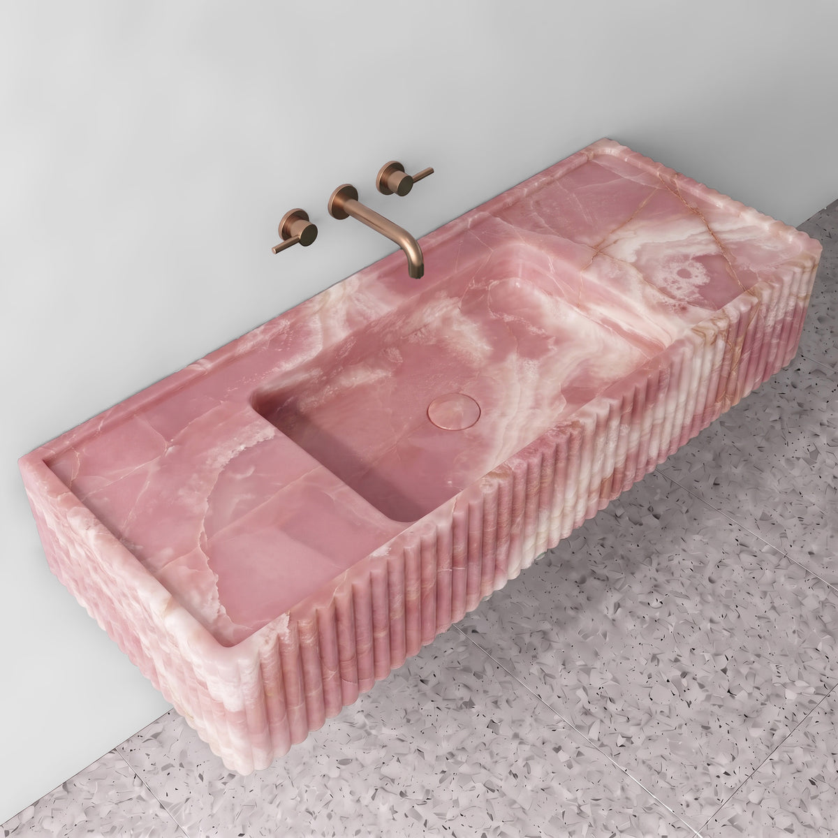 Elevated three-quarter angle of the Pink Onyx fluted monolith sink showing the integrated trough basin, matching stone drain cover, raised perimeter edge, and reeded side detailing.