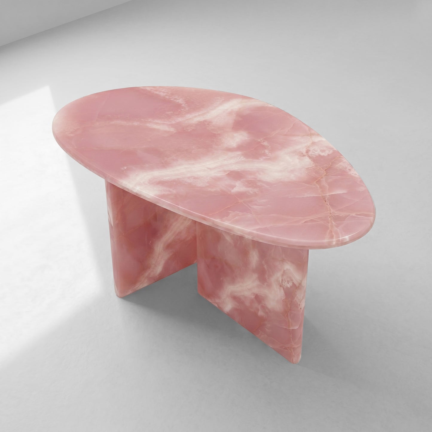 High-angle view of a pebble-shaped pink onyx coffee table, emphasizing its unique organic silhouette and the sophisticated natural patterns of the stone.