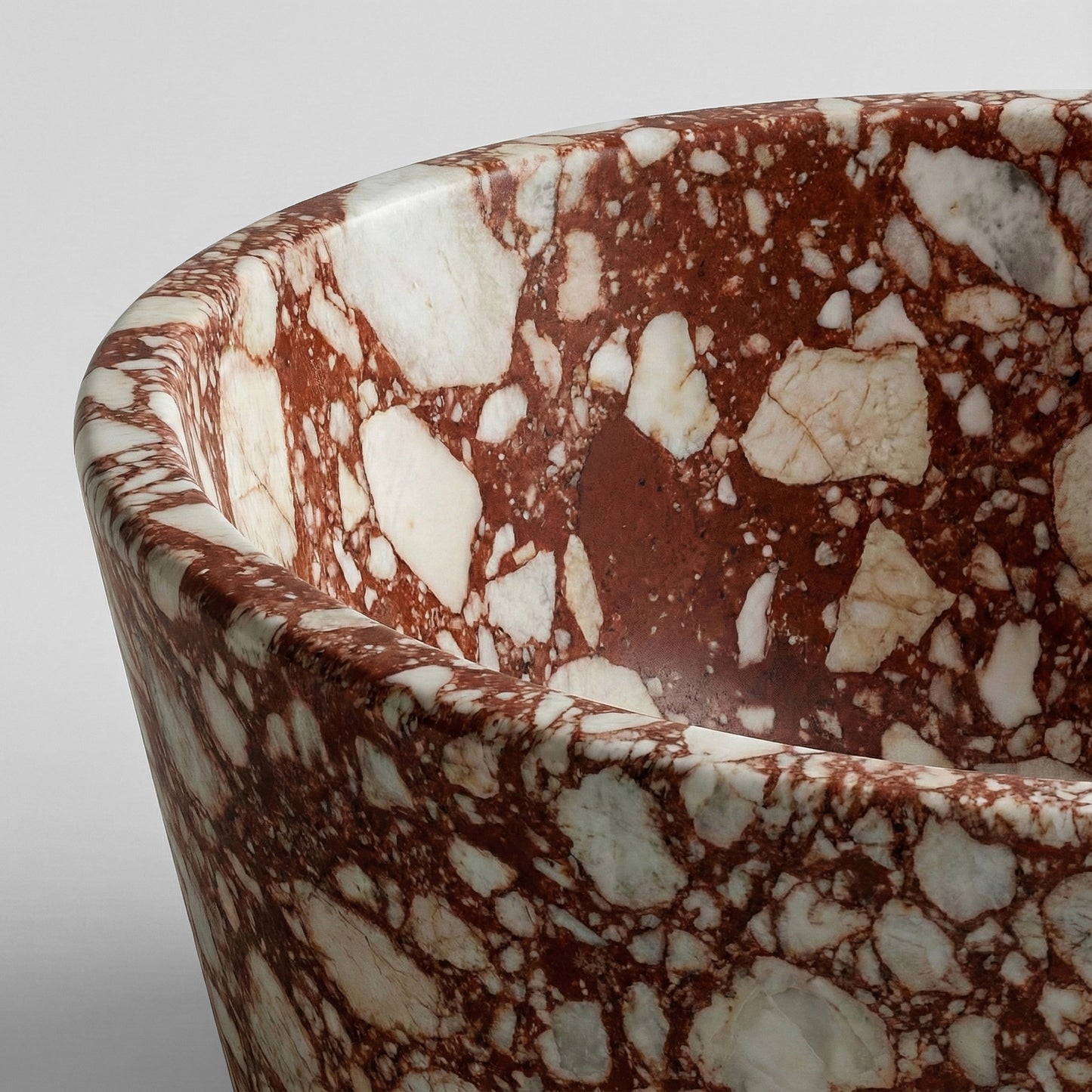 Close-up detail of a Red Bulgari marble bathtub rim showcasing a highly brecciated texture with large white stone fragments set in a deep red matrix.
