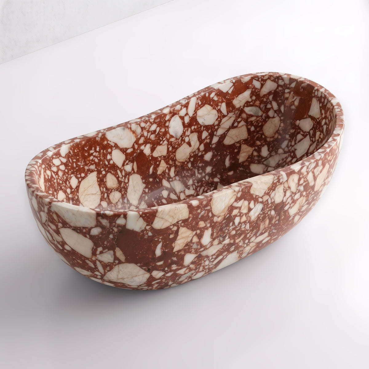 Elevated three-quarter perspective view of the Red Bulgari marble wave soaking tub, highlighting the asymmetrical undulating rim, seamless solid-carved interior, and dense aggregate of cream marble fragments in deep claret stone.